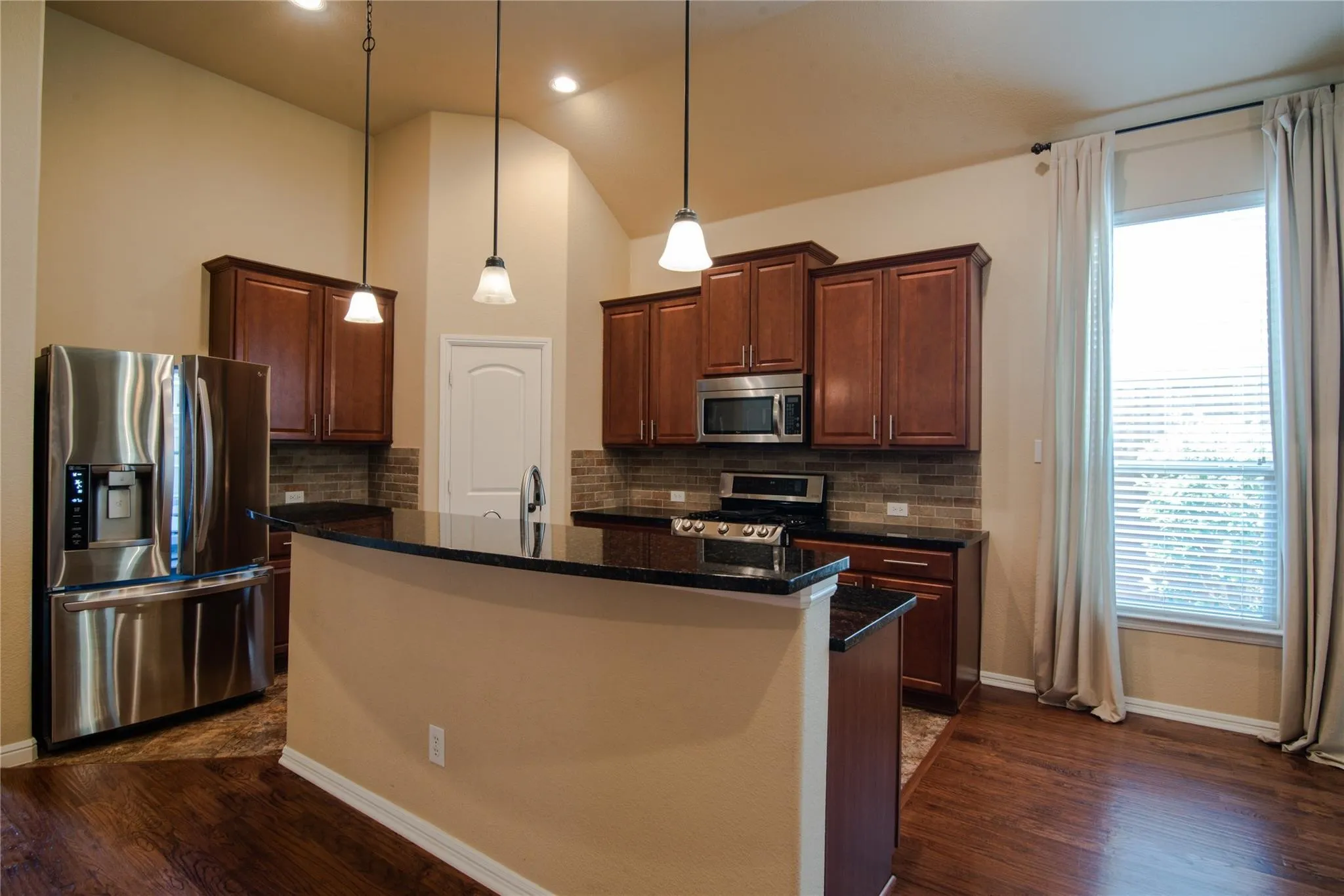 Kitchen with stainless steel appliances, a kitchen island with sink, dark stone countertops, dark wood finished floors, and lofted ceiling