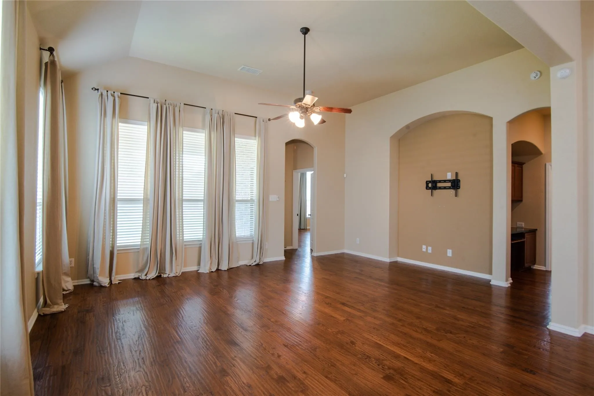 Empty room featuring ceiling fan, dark wood-style flooring, and arched walkways
