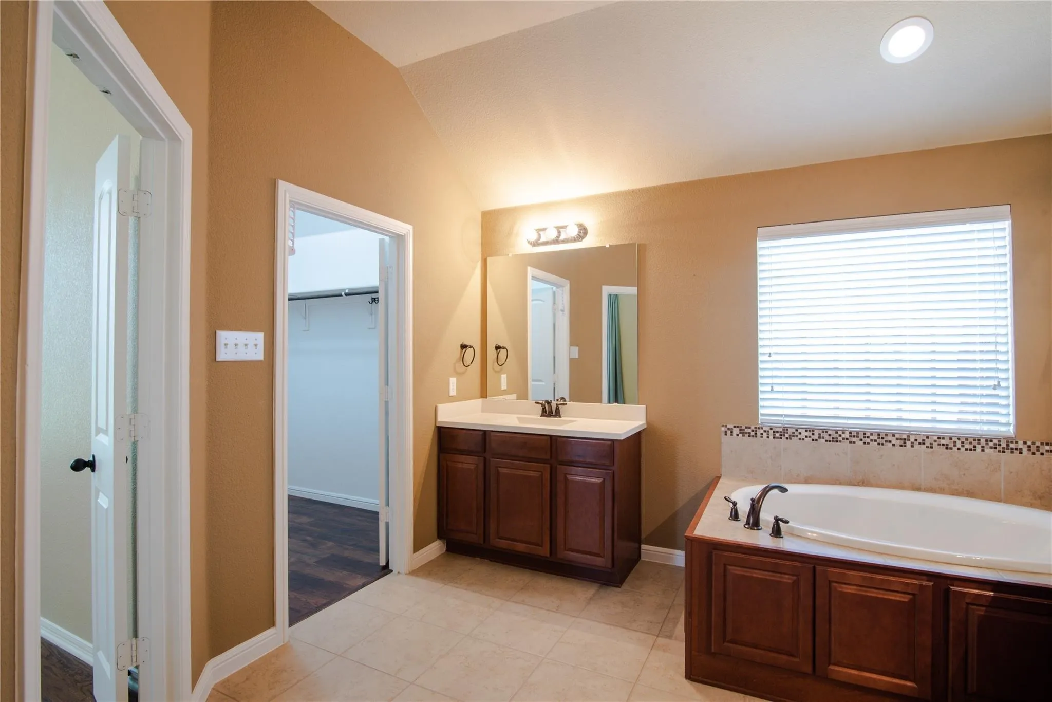 Full bath with a spacious closet, light tile patterned floors, a garden tub, vanity, and lofted ceiling