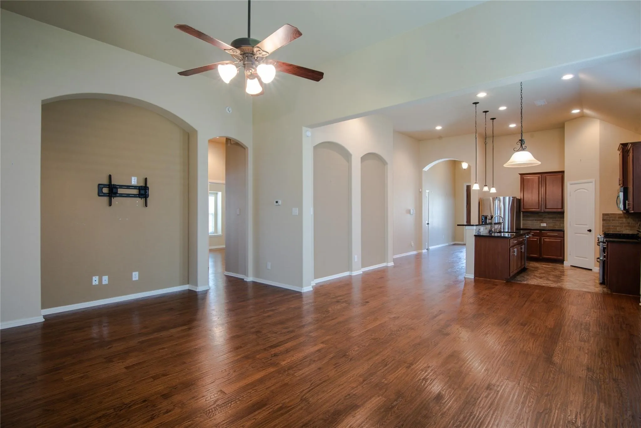 Unfurnished living room featuring dark wood-type flooring, ceiling fan, arched walkways, and recessed lighting