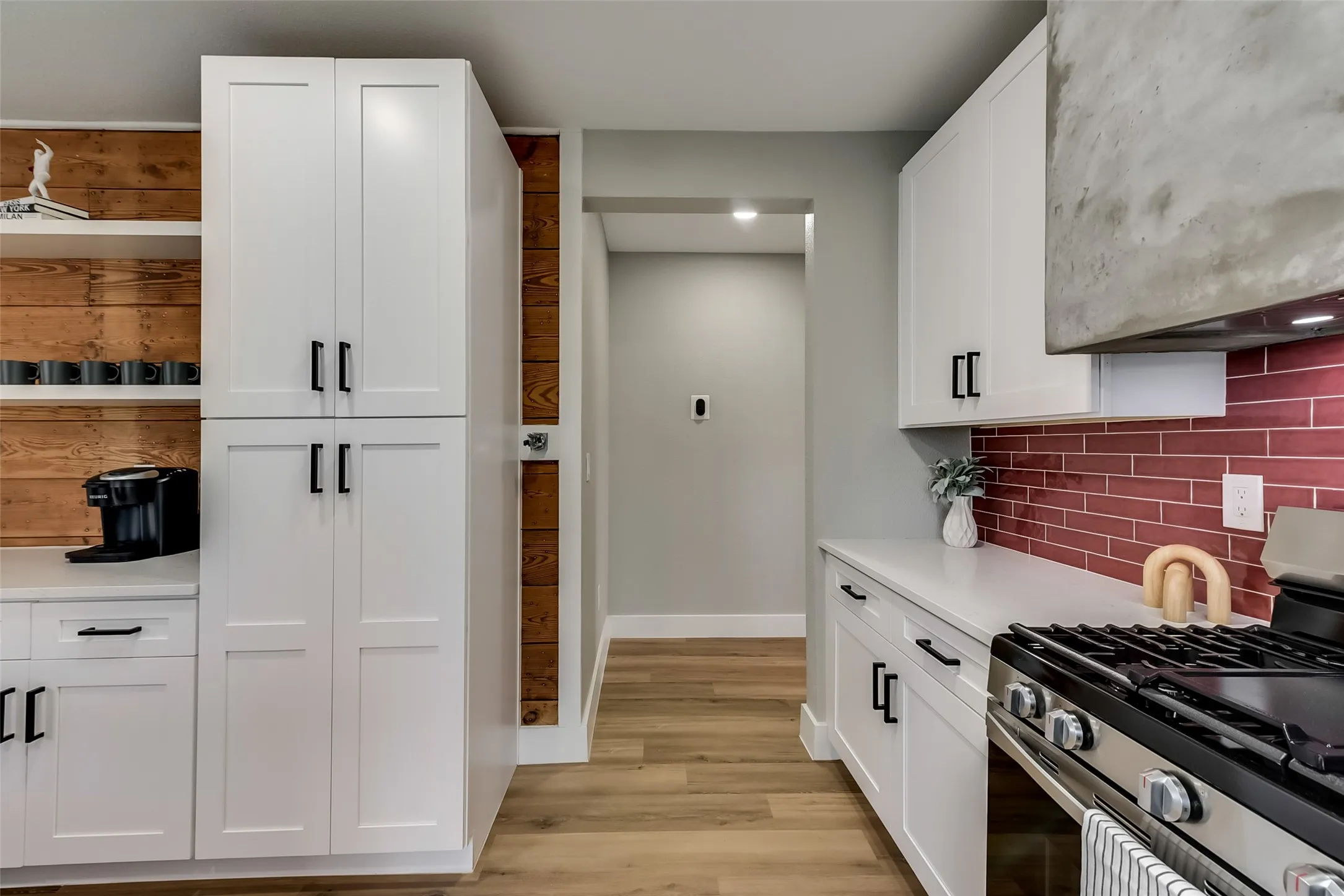 Kitchen with stainless steel gas range, backsplash, light wood-style floors, light countertops, and white cabinets
