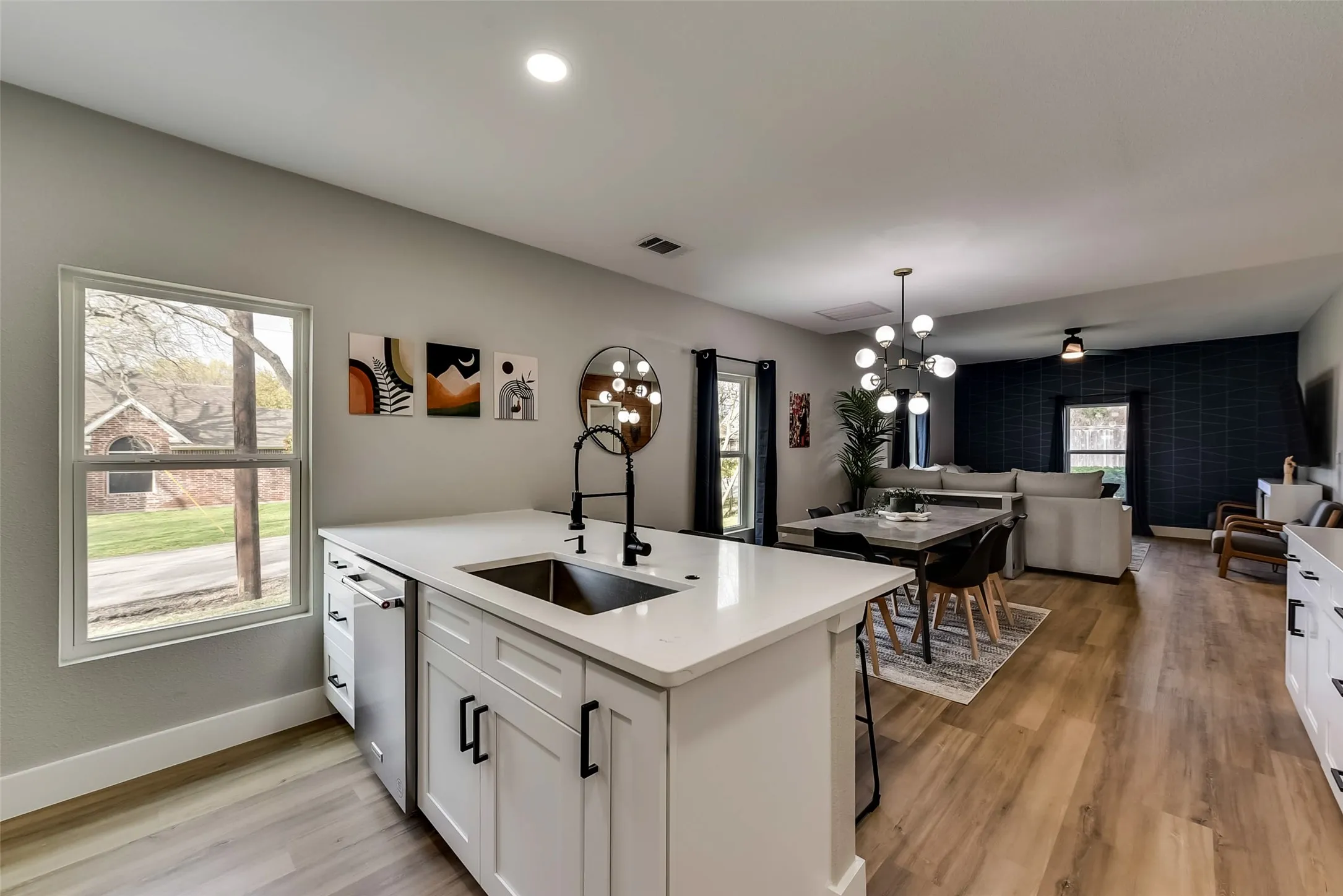Kitchen featuring dishwasher, visible vents, a sink, open floor plan, and white cabinets