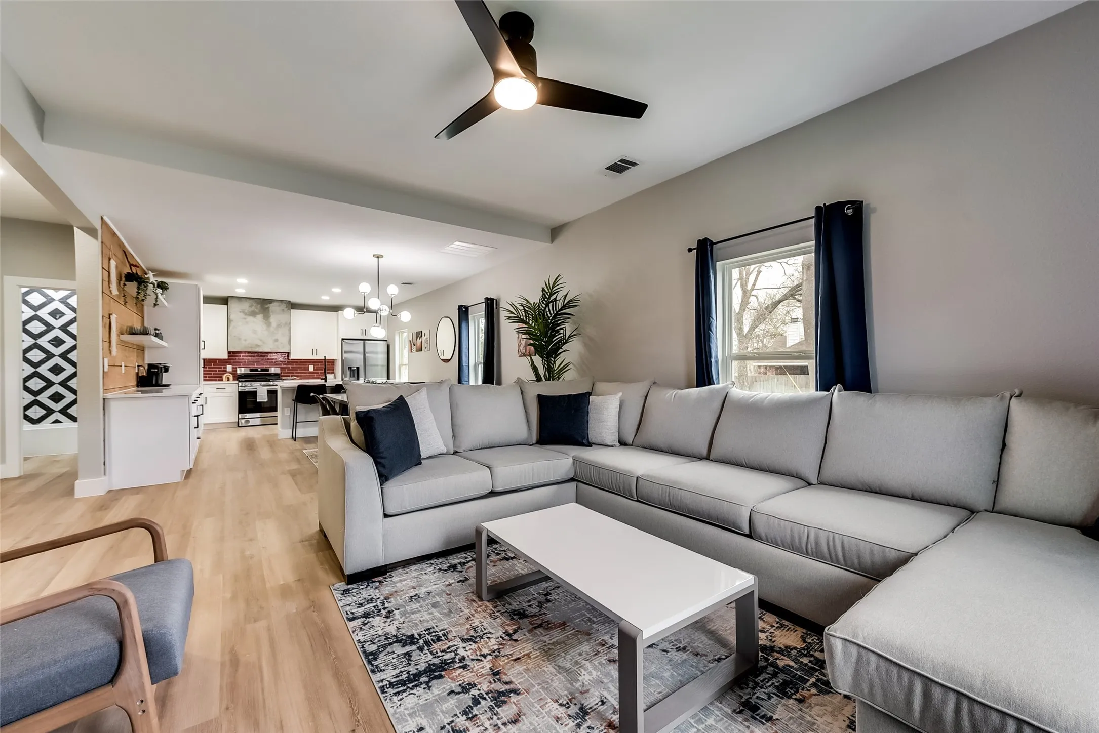 Living room featuring light wood-style floors, visible vents, ceiling fan with notable chandelier, and recessed lighting
