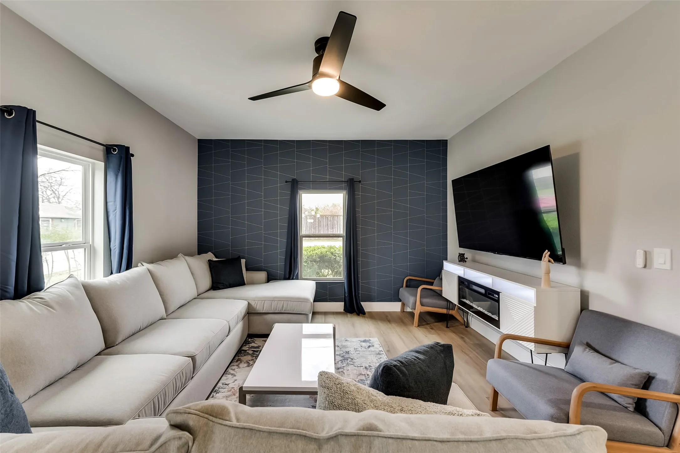 Living area with an accent wall, ceiling fan, plenty of natural light, and wood finished floors