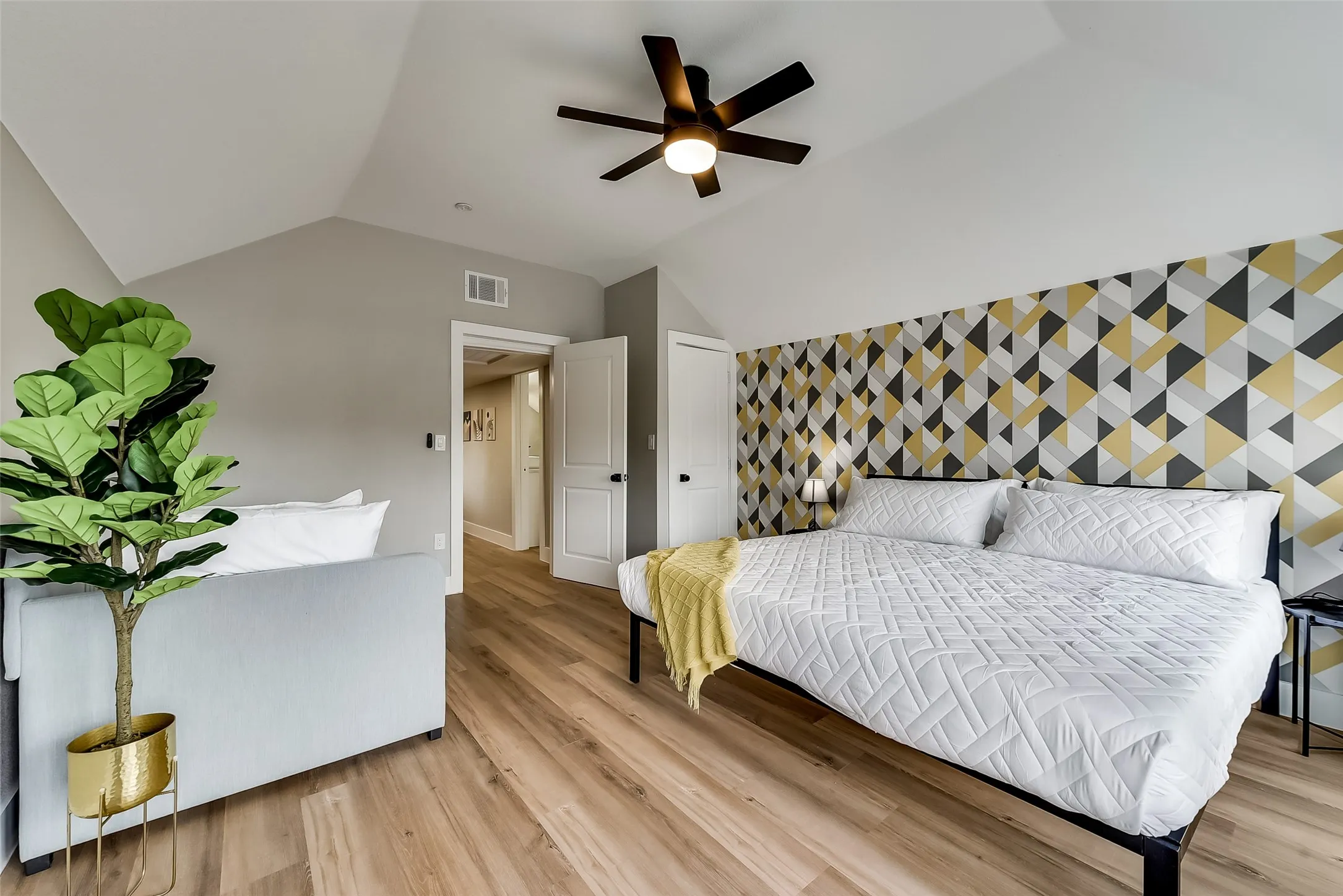 Bedroom featuring light wood-style floors, visible vents, lofted ceiling, and an accent wall