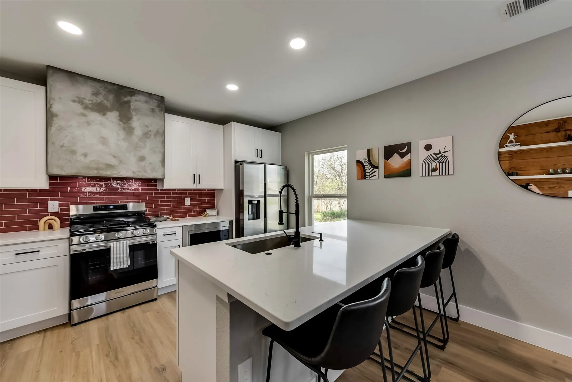 Kitchen with light wood-style flooring, a kitchen bar, backsplash, light countertops, and appliances with stainless steel finishes