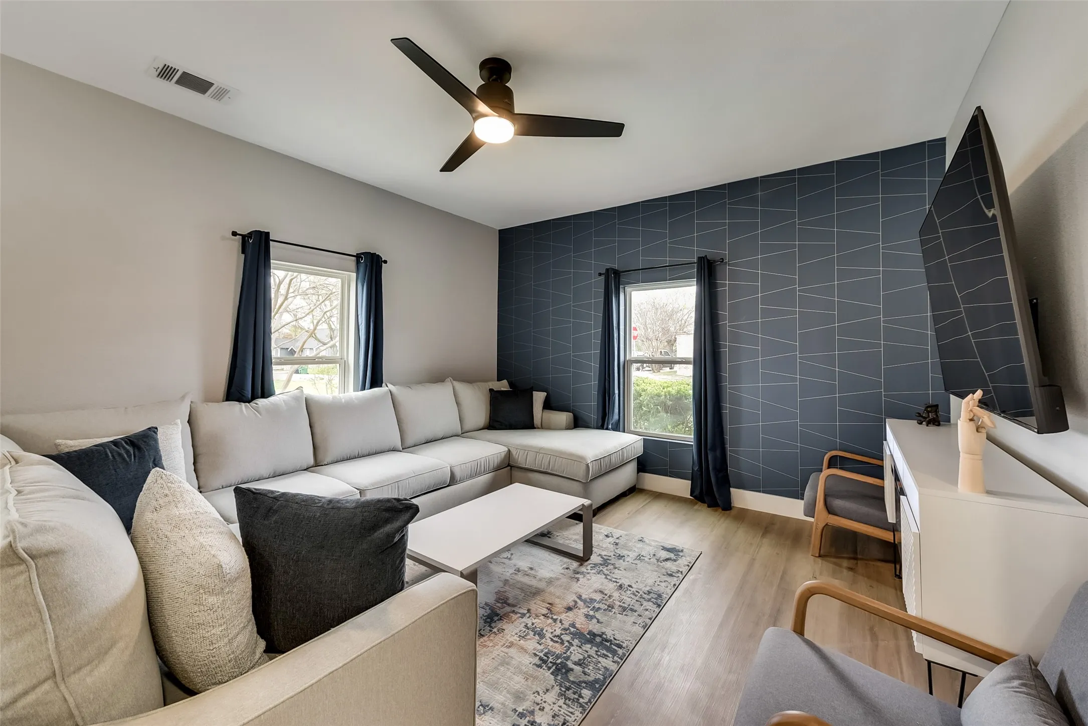 Living room with ceiling fan, tile walls, light wood finished floors, and visible vents