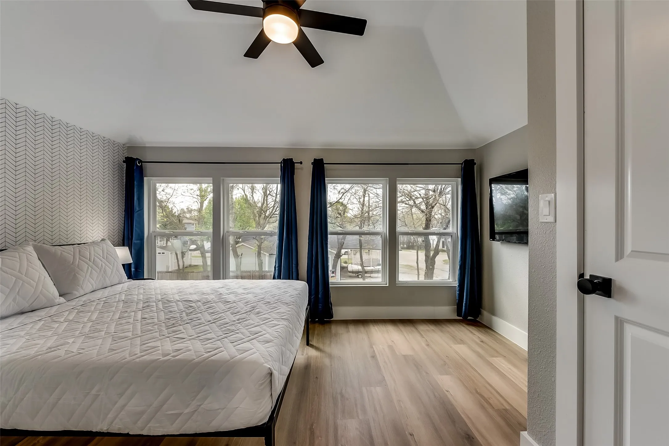 Bedroom with vaulted ceiling, wallpapered walls, baseboards, an accent wall, and wood finished floors