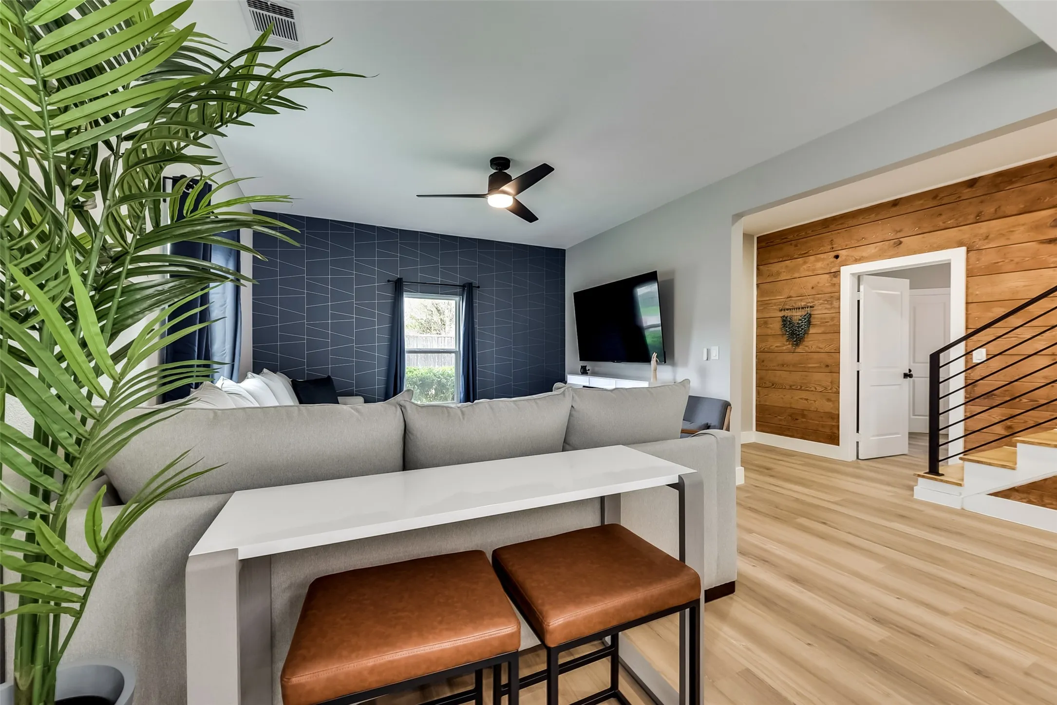 Living area with a ceiling fan, baseboards, stairs, an accent wall, and light wood-type flooring