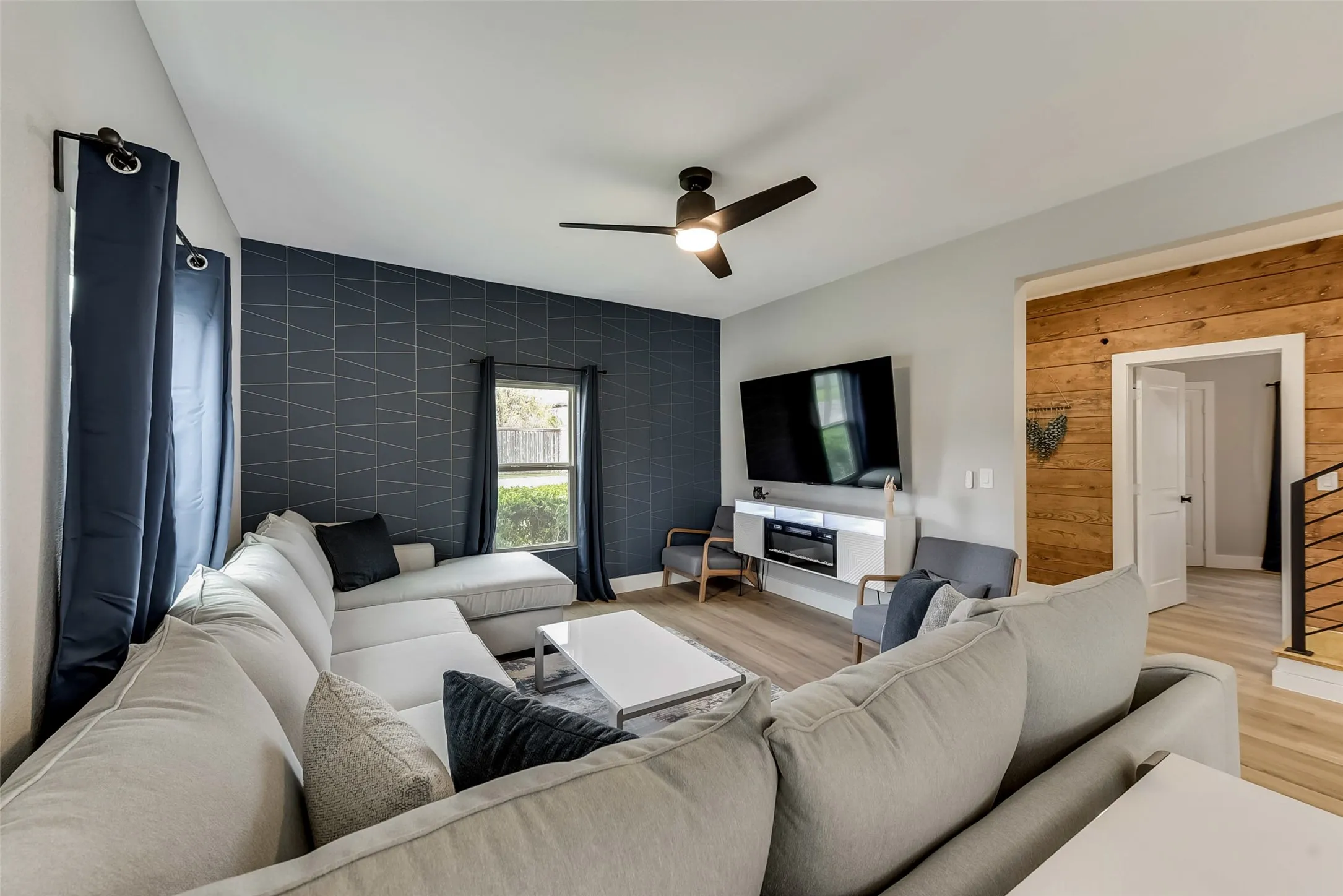 Living room featuring light wood-style flooring, wood walls, baseboards, ceiling fan, and an accent​​‌​​​​‌​​‌‌​‌‌​​​‌‌​‌​‌​‌​​​‌​​ wall