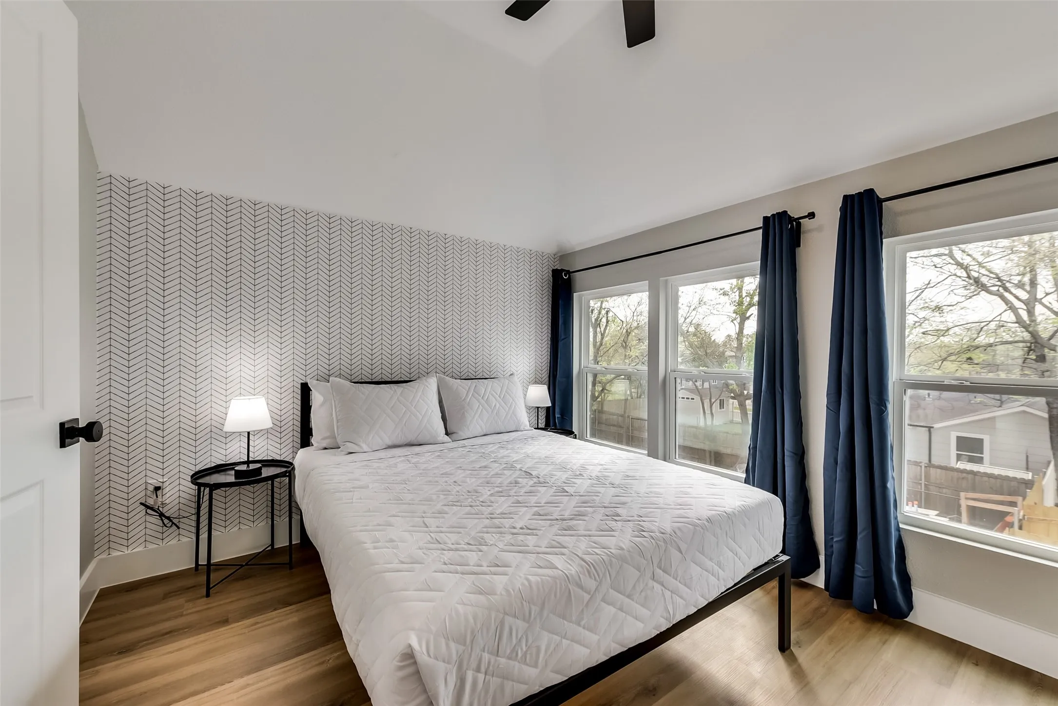 Bedroom featuring wallpapered walls, vaulted ceiling, baseboards, and an accent wall