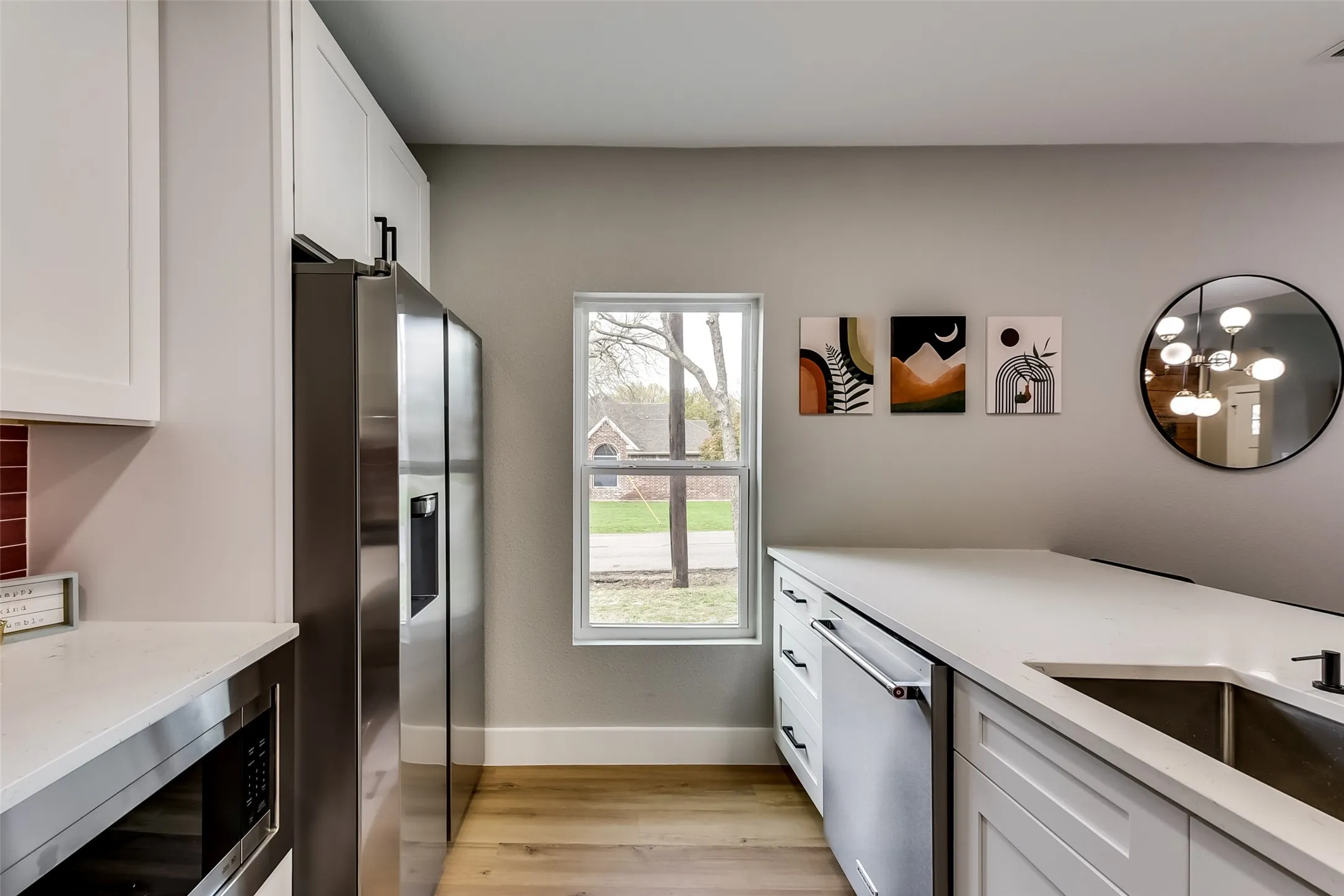 Kitchen featuring a sink, stainless steel appliances, white cabinets, light wood-type flooring, and baseboards