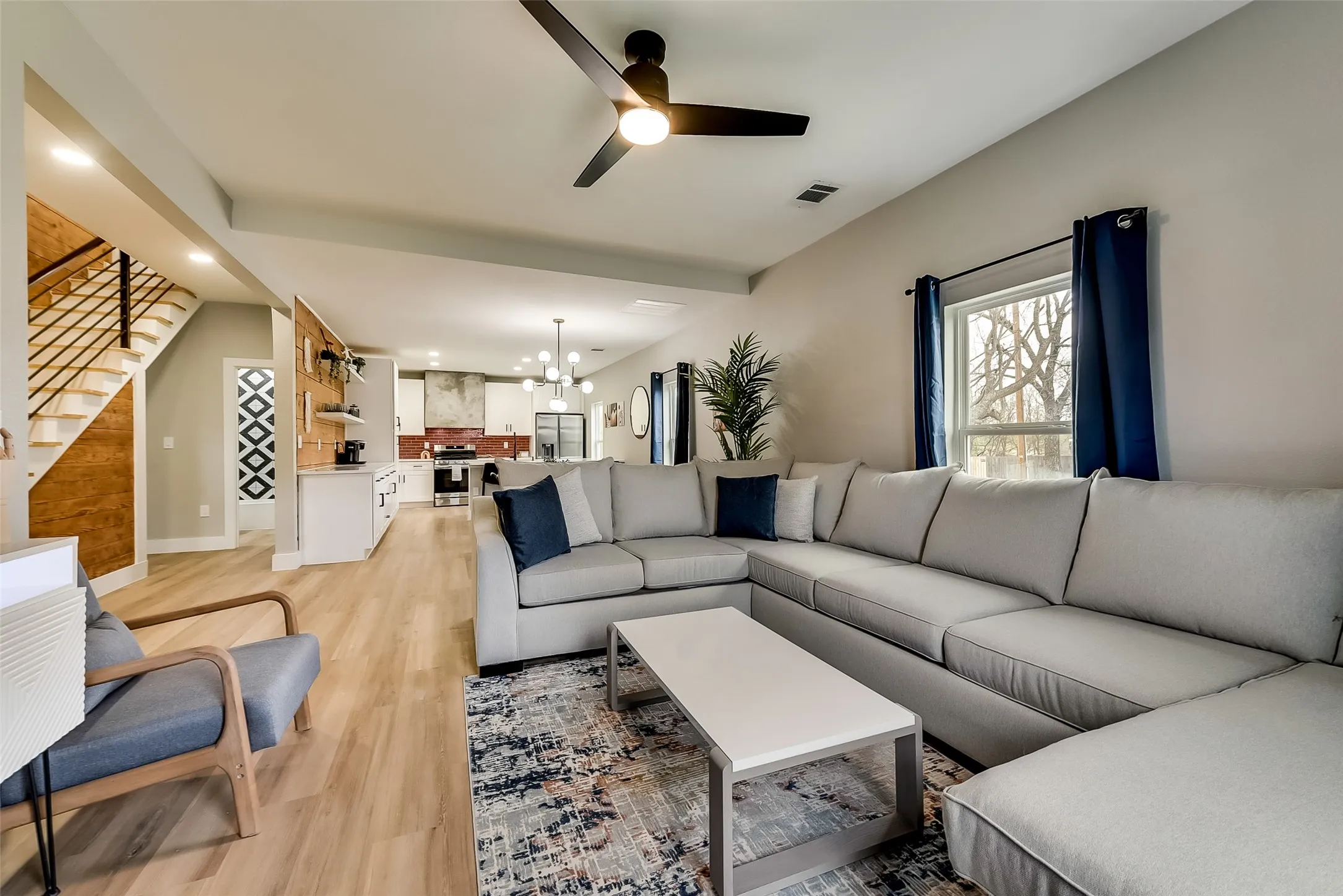 Living room featuring ceiling fan with notable chandelier, light wood-type flooring, visible vents, recessed lighting, and stairway