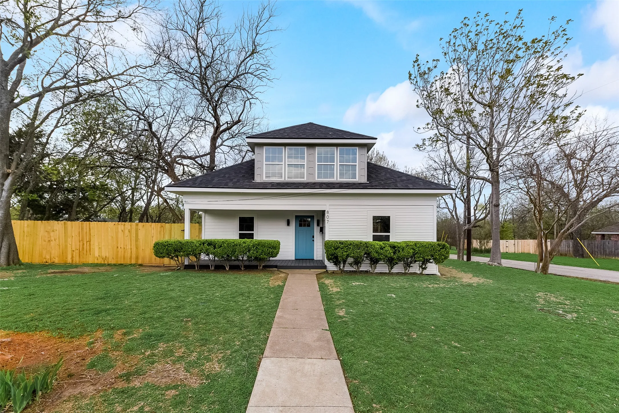 Bungalow featuring covered porch, roof with shingles, fence, and a front lawn