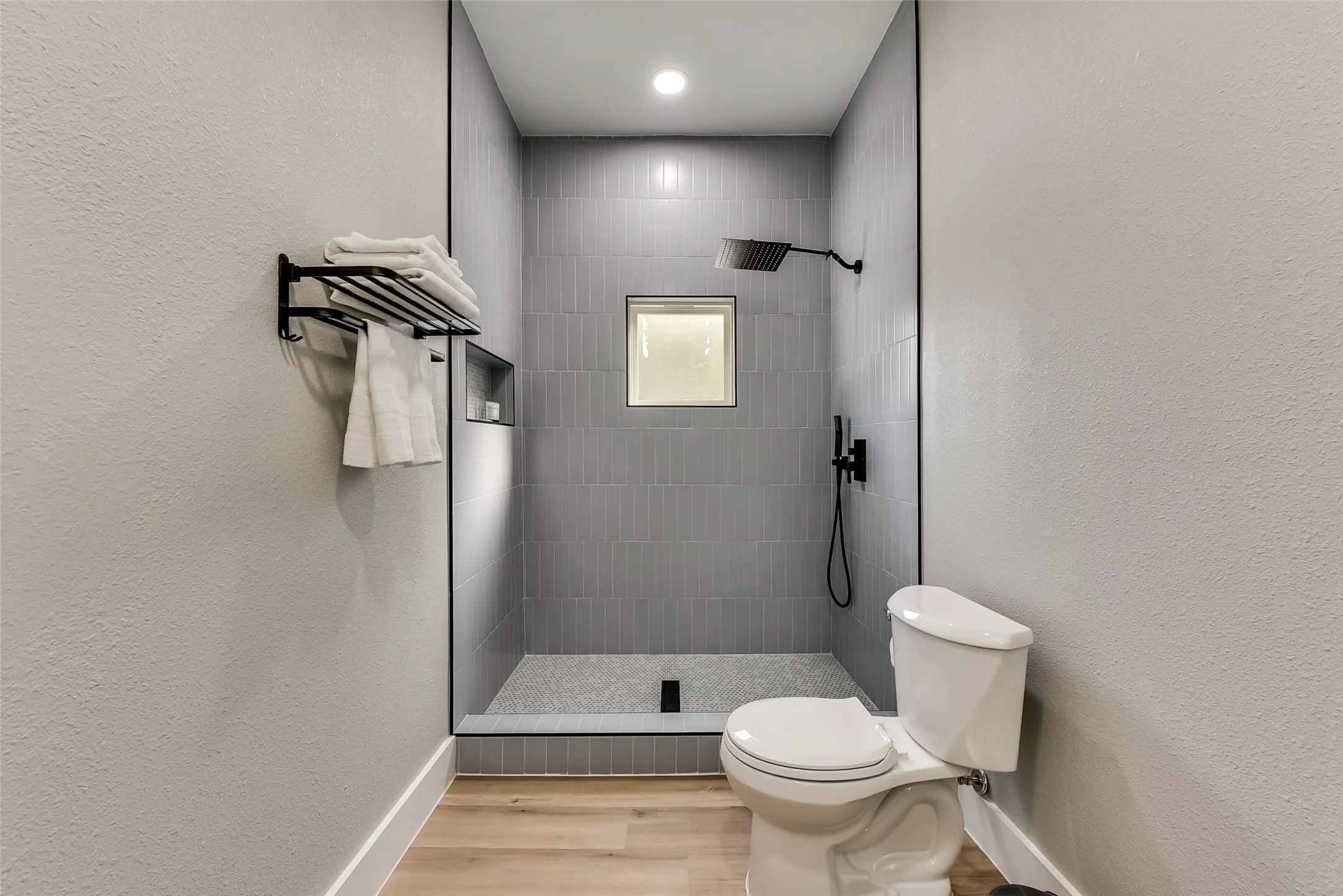 Bathroom featuring toilet, wood finished floors, recessed lighting, baseboards, and tiled shower