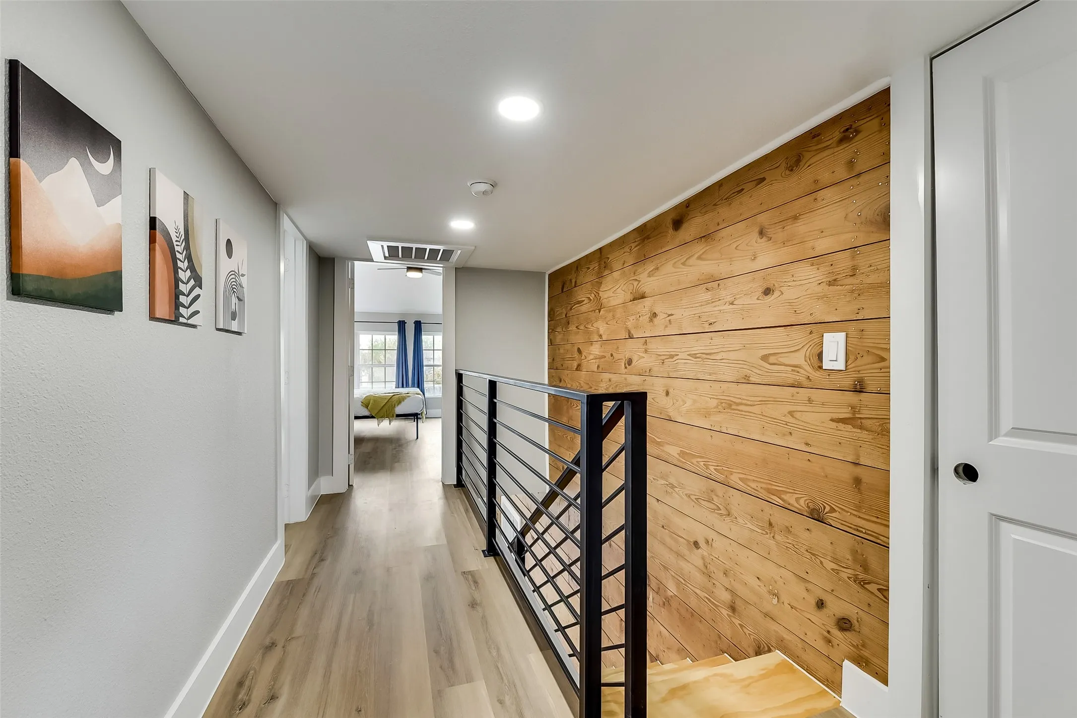 Hall with baseboards, light wood finished floors, visible vents, wooden walls, and an upstairs landing