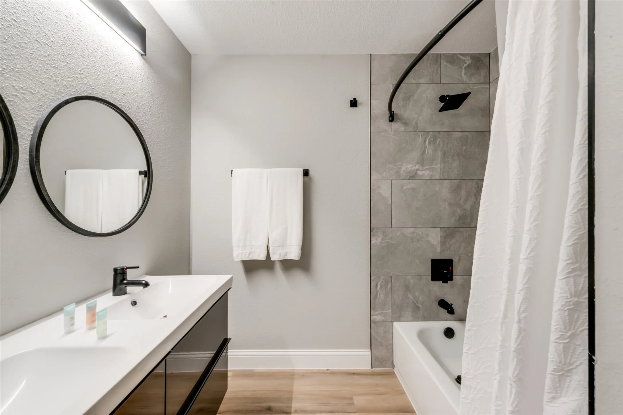 Bathroom with wood finished floors, shower / bath combination with curtain, double vanity, and a textured ceiling