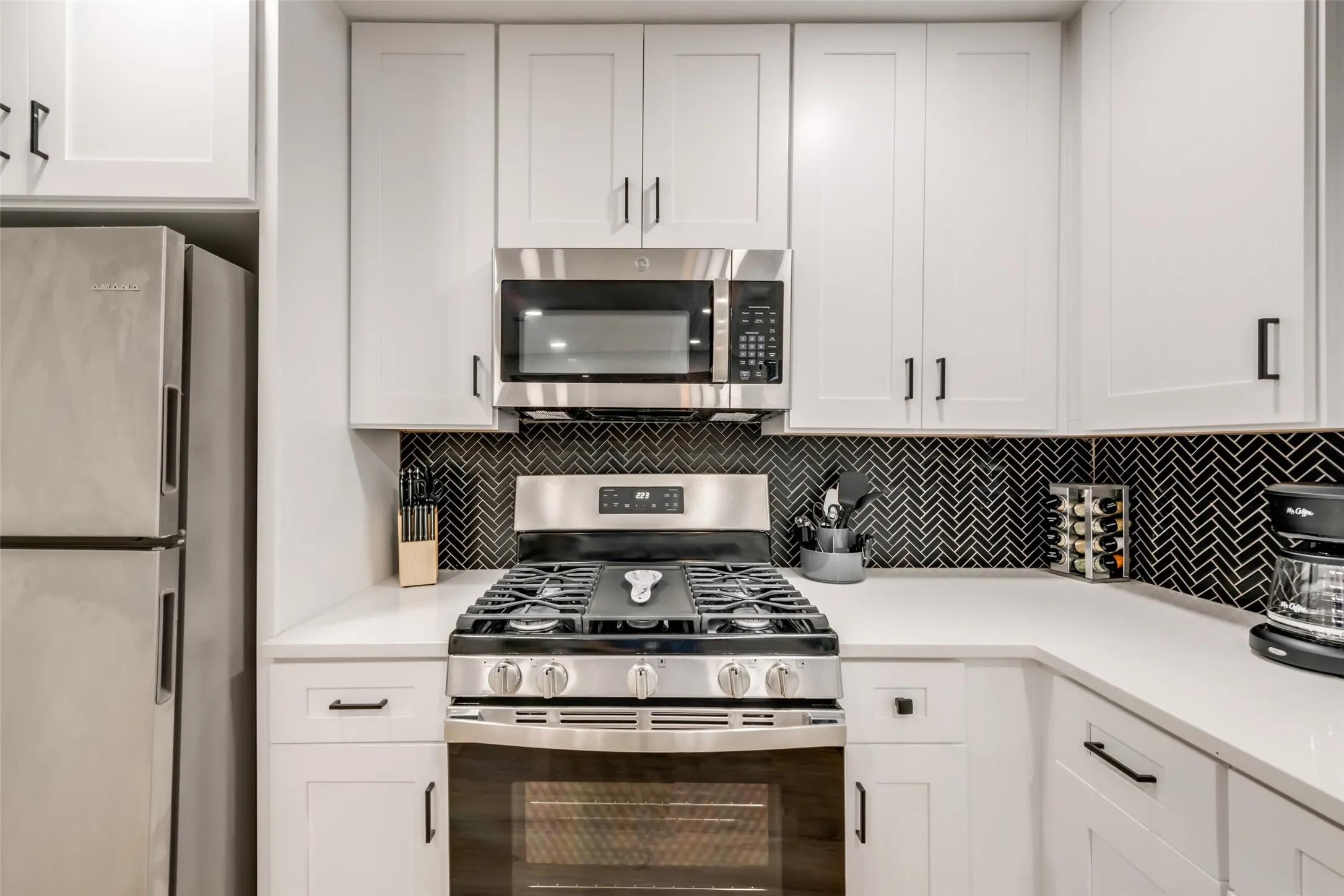 Kitchen featuring stainless steel appliances, decorative backsplash, white cabinets, and light countertops