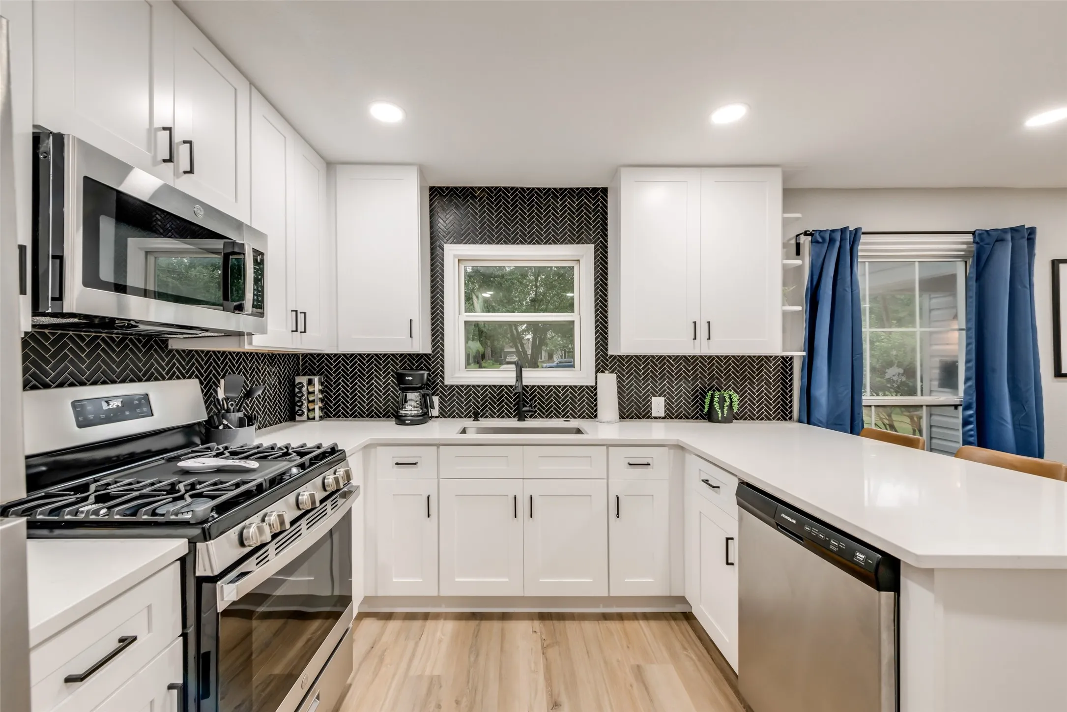 Kitchen featuring appliances with stainless steel finishes, a peninsula, recessed lighting, light countertops, and white cabinets