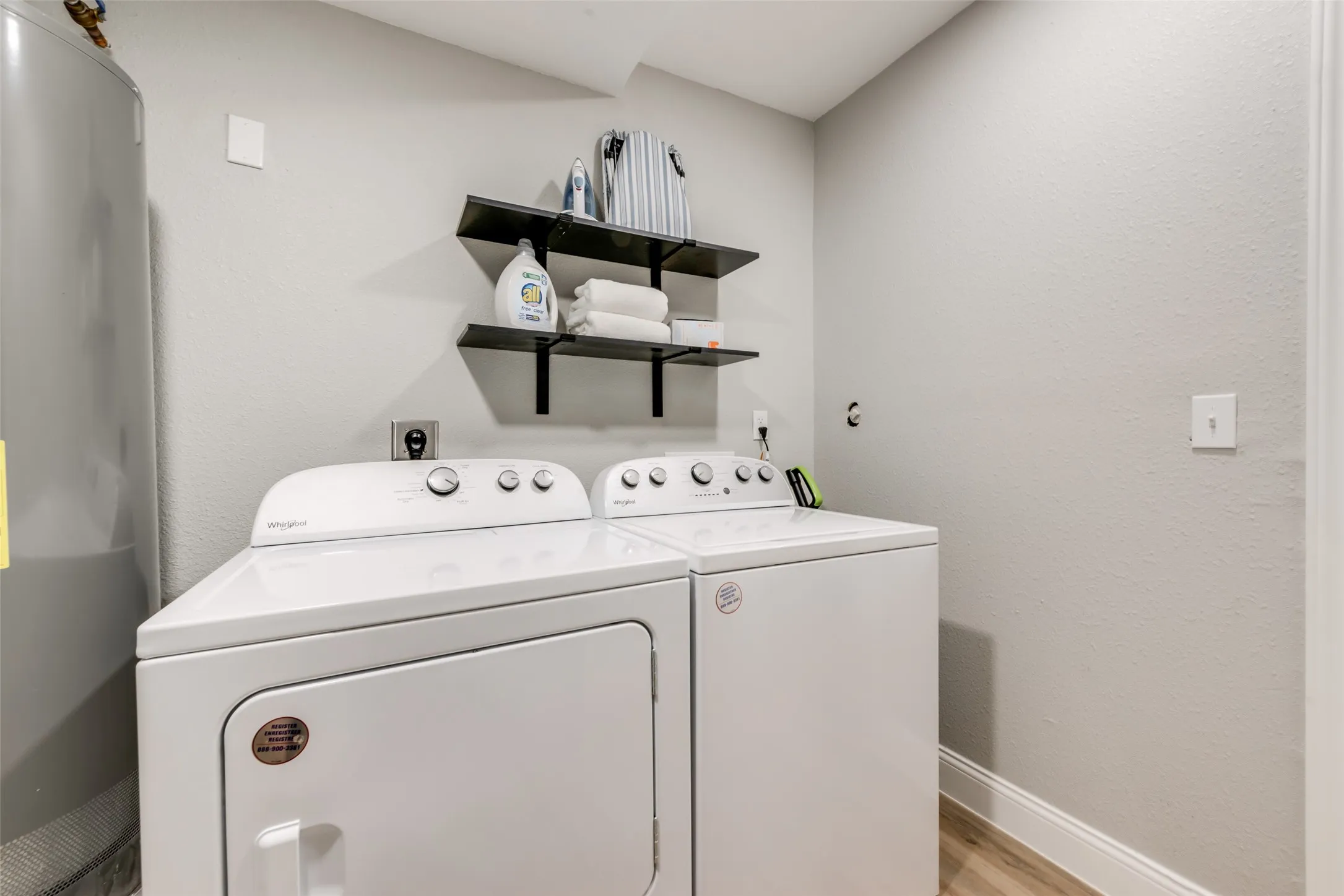 Laundry room with washer and dryer, water heater, a textured wall, and light wood-style flooring