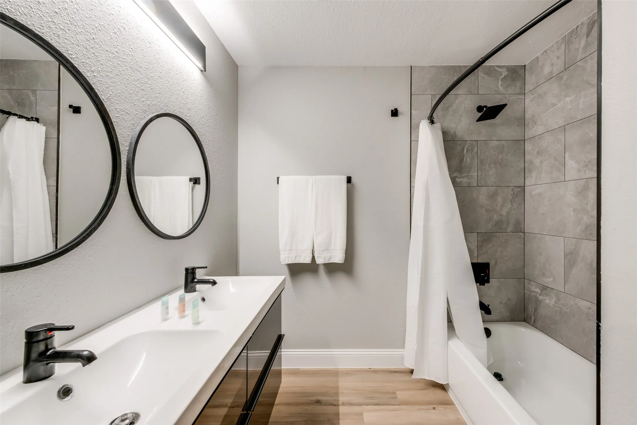Bathroom featuring wood finished floors, shower / bath combo, double vanity, and a textured ceiling