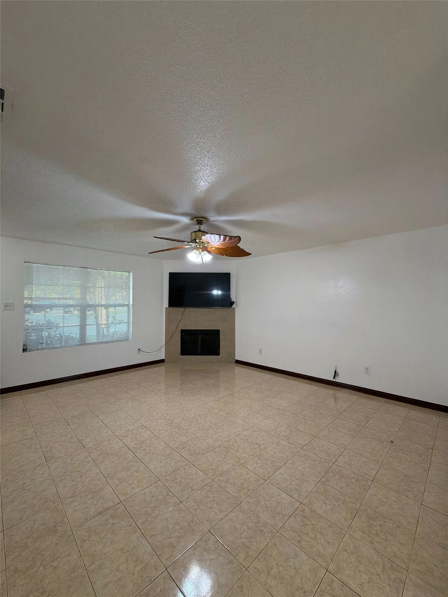 Unfurnished living room featuring ceiling fan, a fireplace, a textured ceiling, and light tile patterned floors