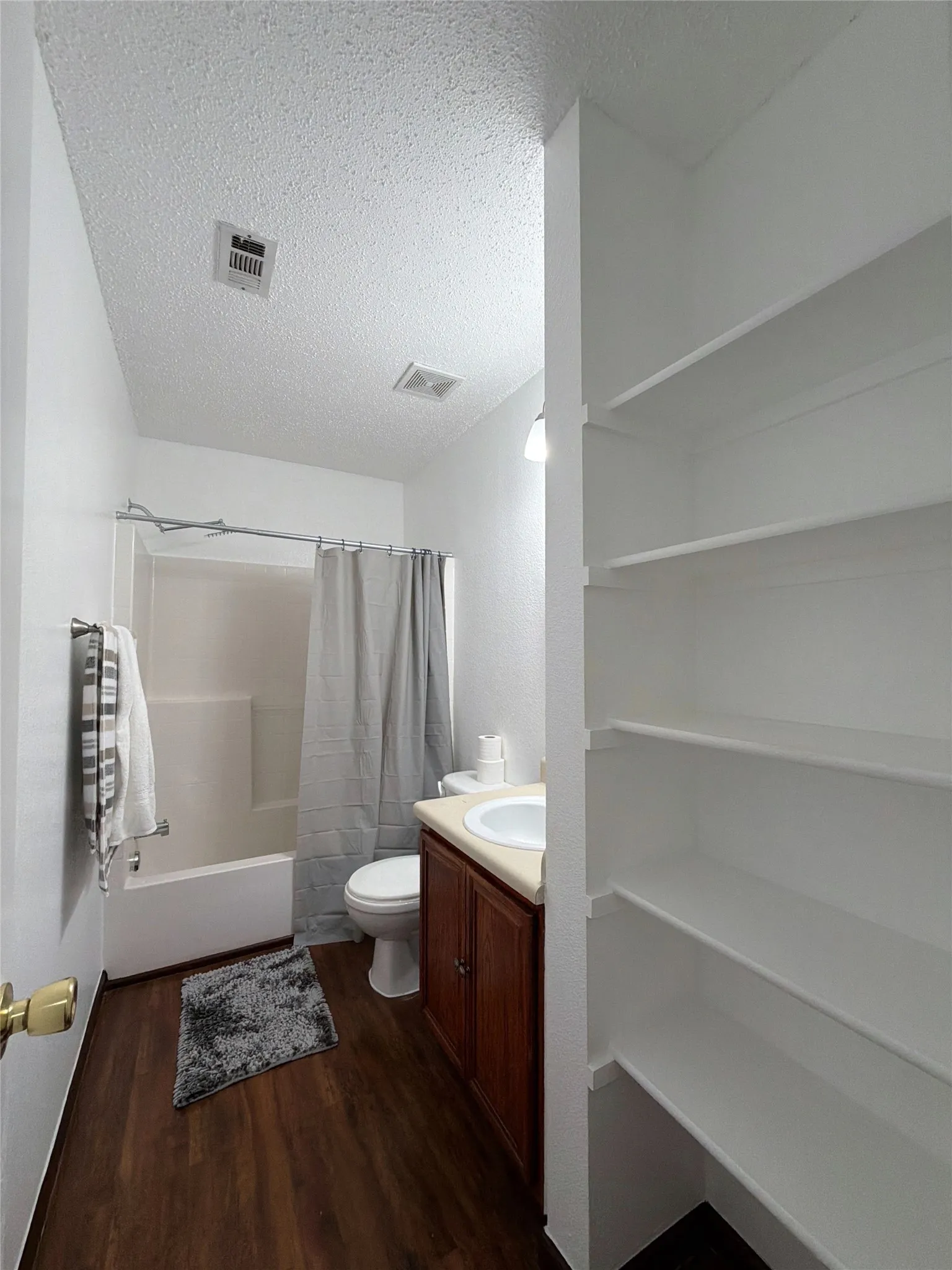 Hallway full bath featuring vanity, a textured ceiling, dark wood-style floors, and shower / bath combination with curtain