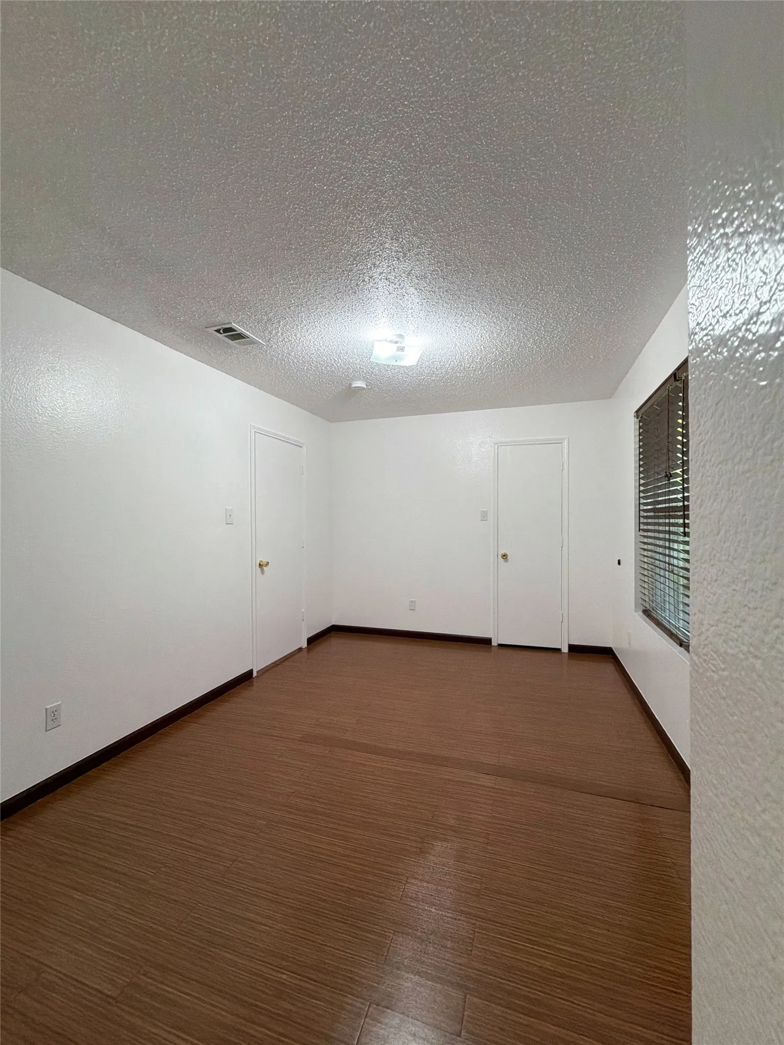 Spare room featuring a textured ceiling, dark wood-style floors, and a textured wall