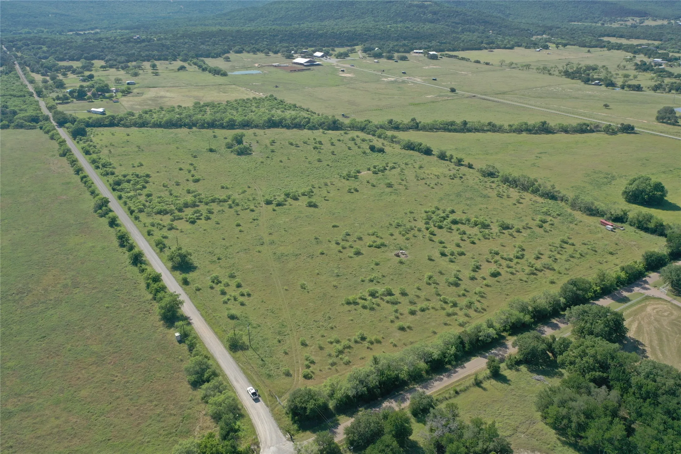 Expansive acreage featuring a perimeter of mature trees, a long road frontage, and a partially cleared interior with scattered brush