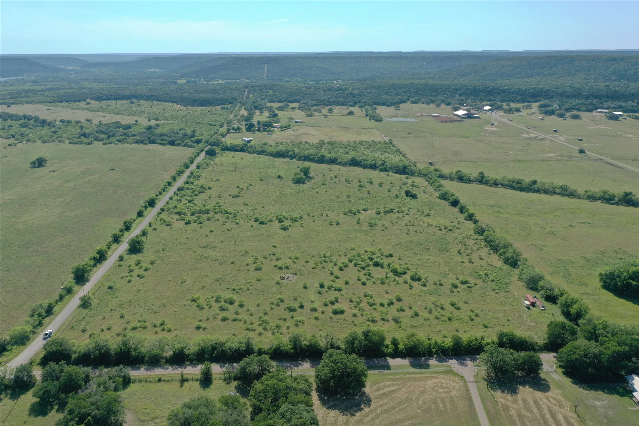 Expansive land parcel featuring a paved road frontage, mature tree lines, and distant natural landscapes