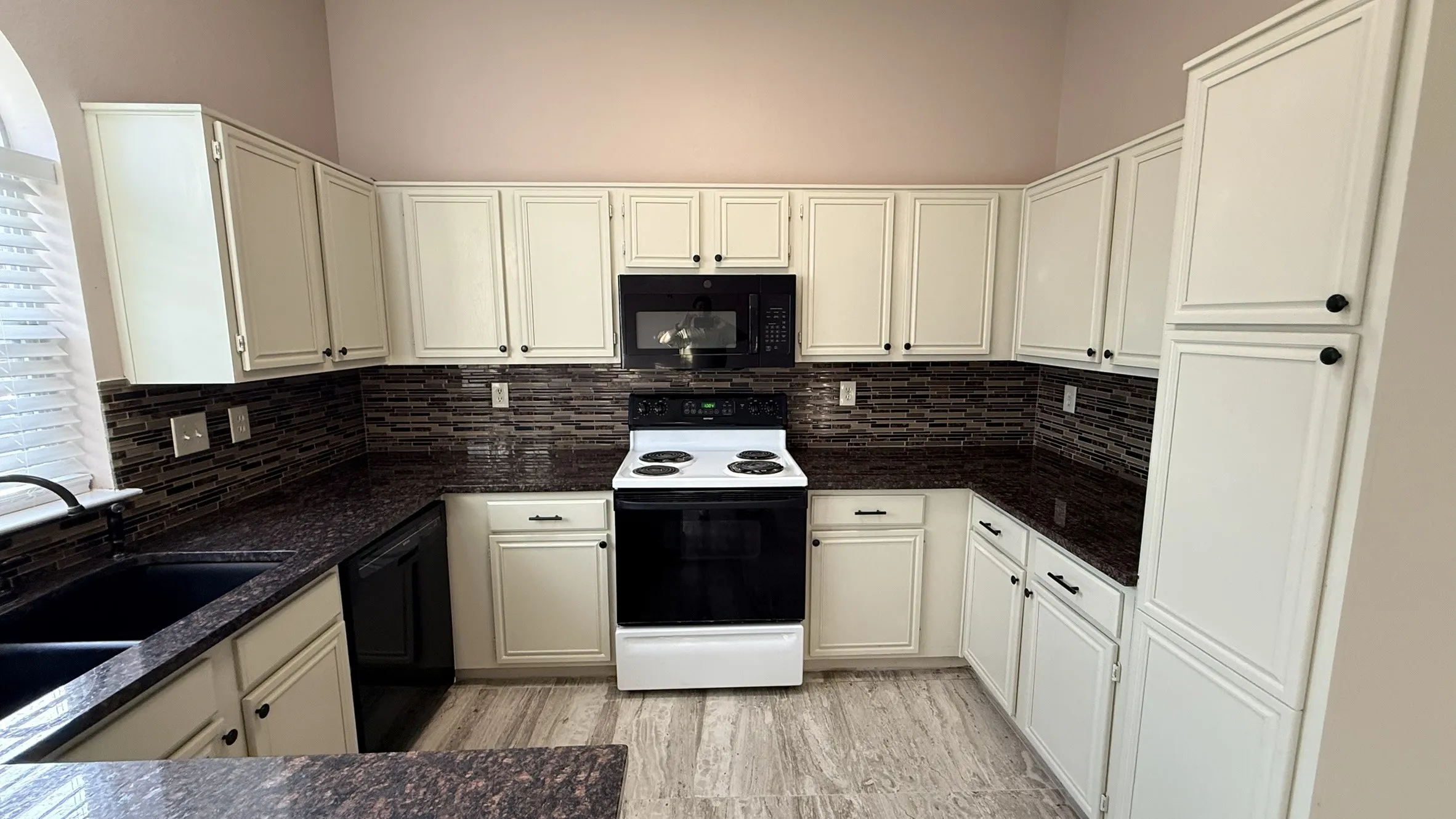 Kitchen with black appliances, tasteful backsplash, dark stone countertops, and white cabinets