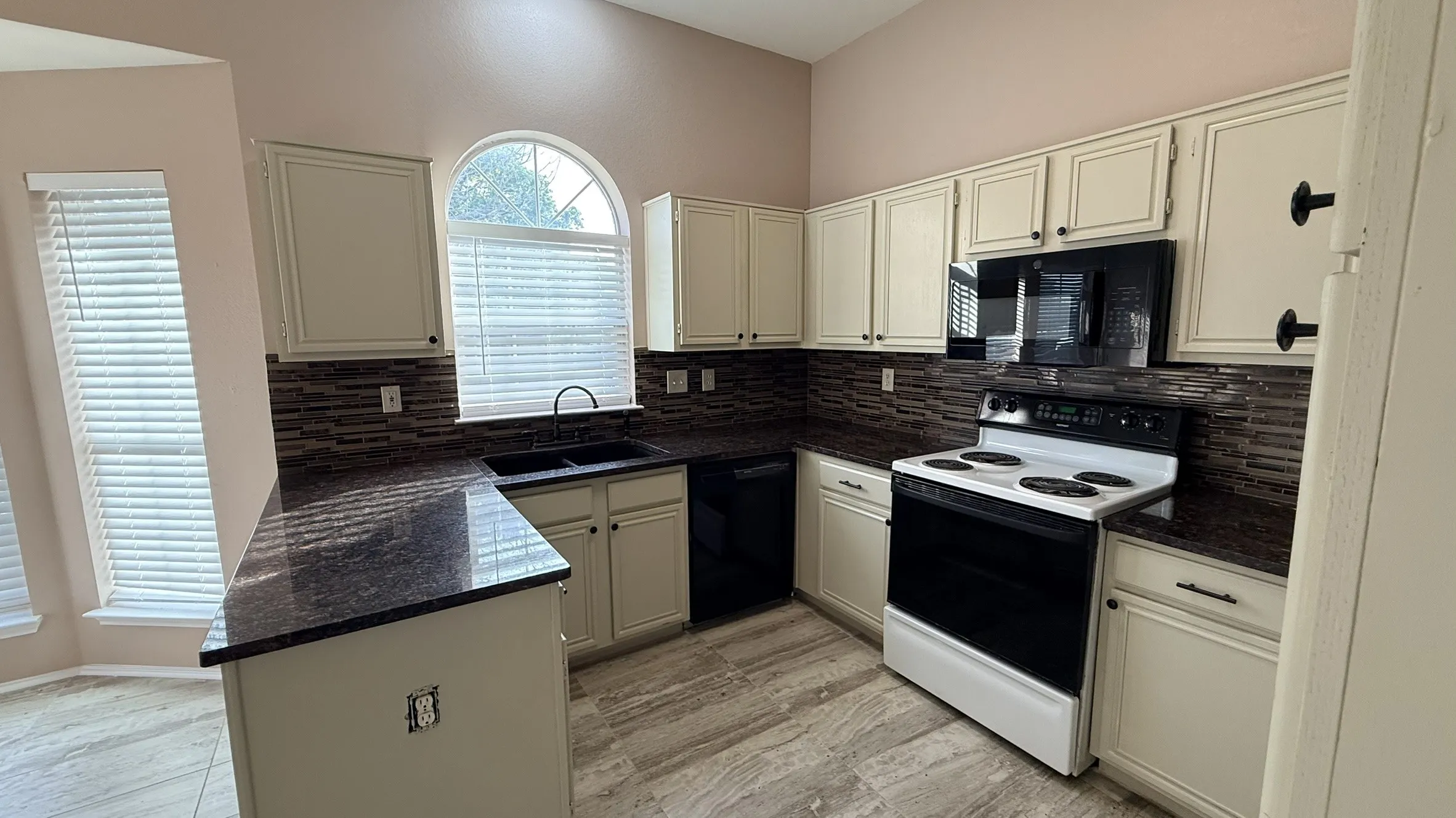 Kitchen with black appliances, dark stone countertops, a peninsula, and backsplash
