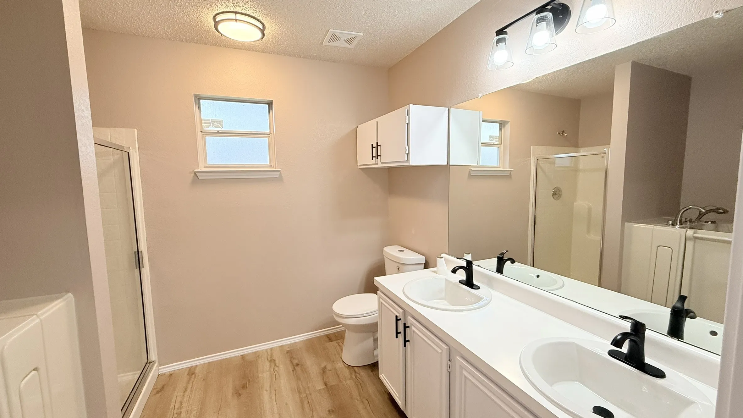 Bathroom featuring a textured ceiling, a shower stall, double vanity, light wood finished floors, and a garden tub