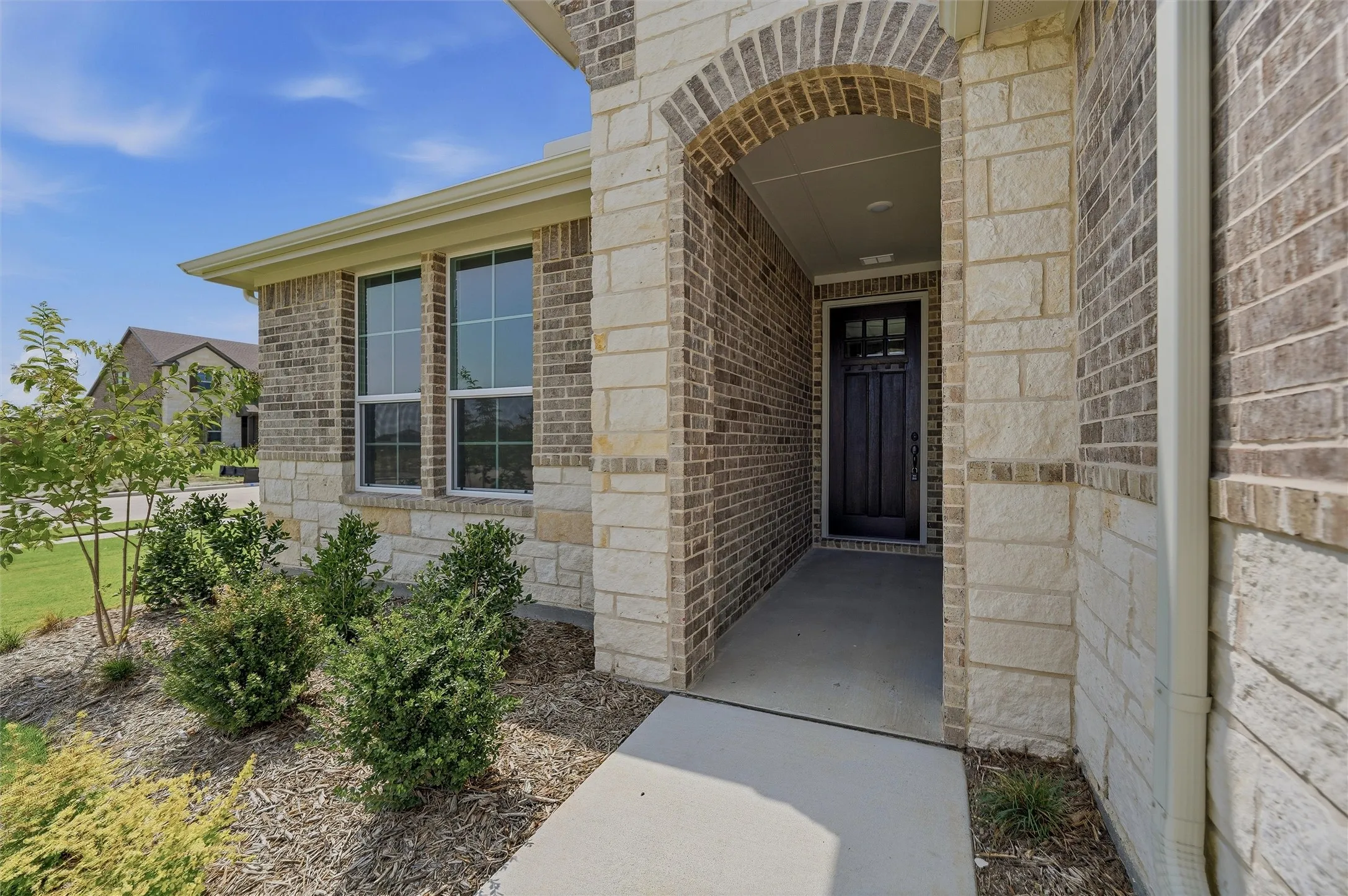 Brick and stone exterior with an arched entryway, dark wood-paneled door, and ground-level landscaping