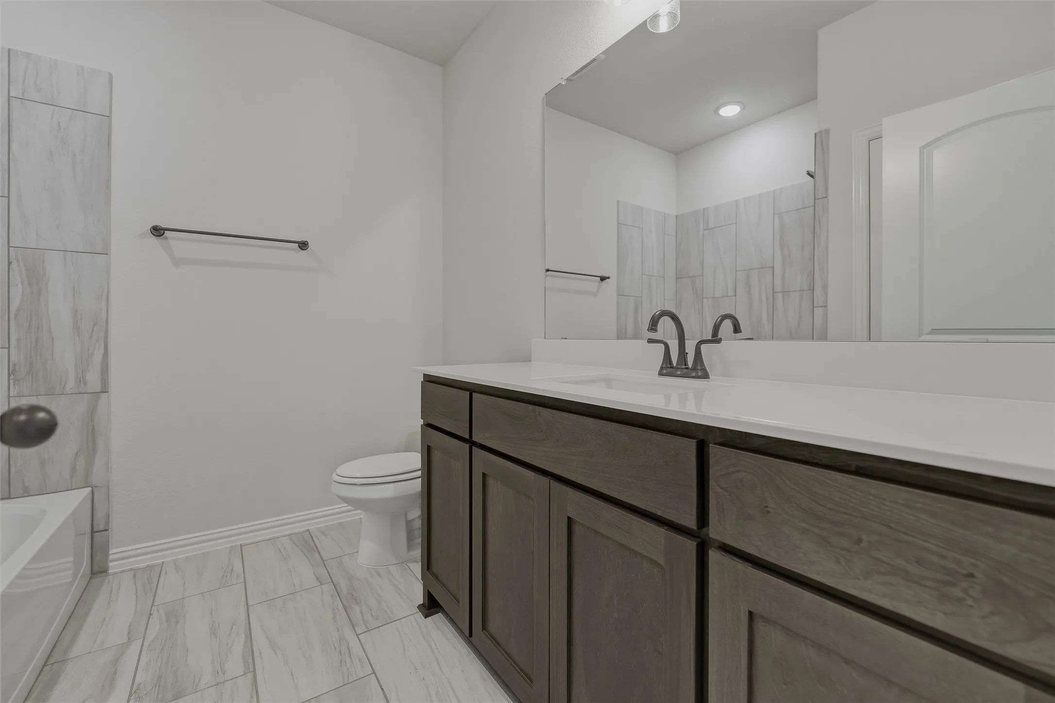 Wood-finish vanity with white countertop, integrated sink, and dark bronze fixtures