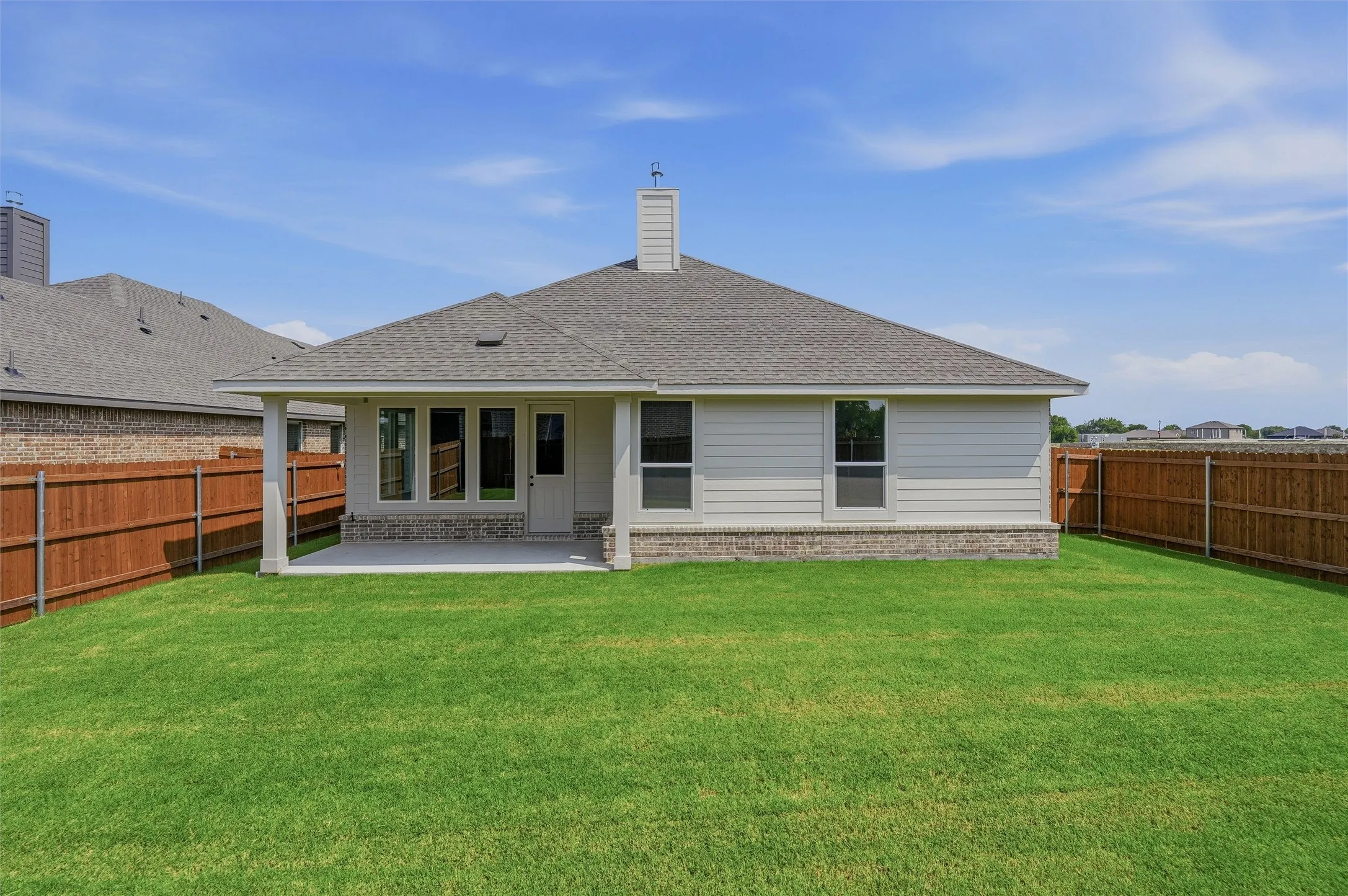 Expansive green lawn, covered patio, privacy fencing, and a chimney feature