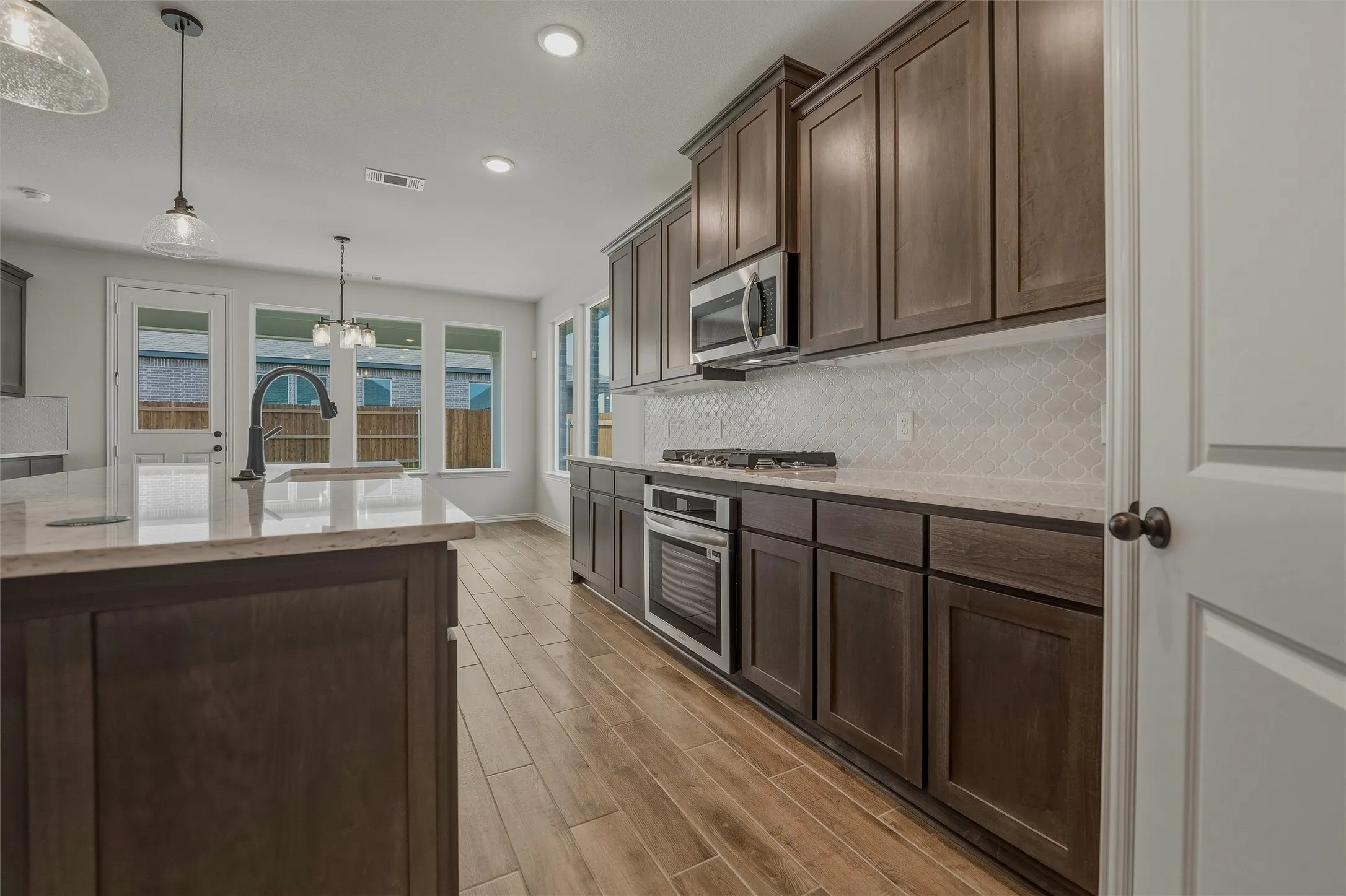 Kitchen featuring wood-finish flooring, dark wood cabinetry, light-toned countertops, a geometric pattern backsplash, and stainless steel appliances