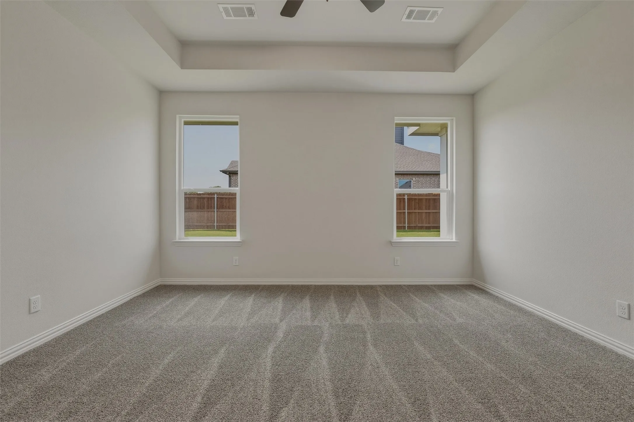 Tray ceiling with recessed lighting, two windows, gray patterned carpet, and white walls