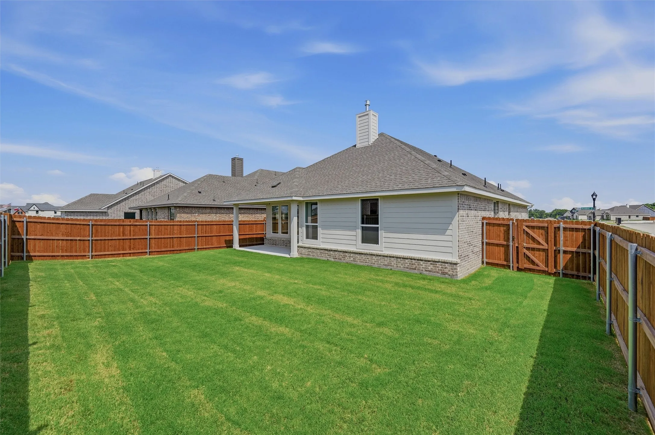 Expansive backyard featuring a manicured lawn, full wood fencing, and a covered patio area