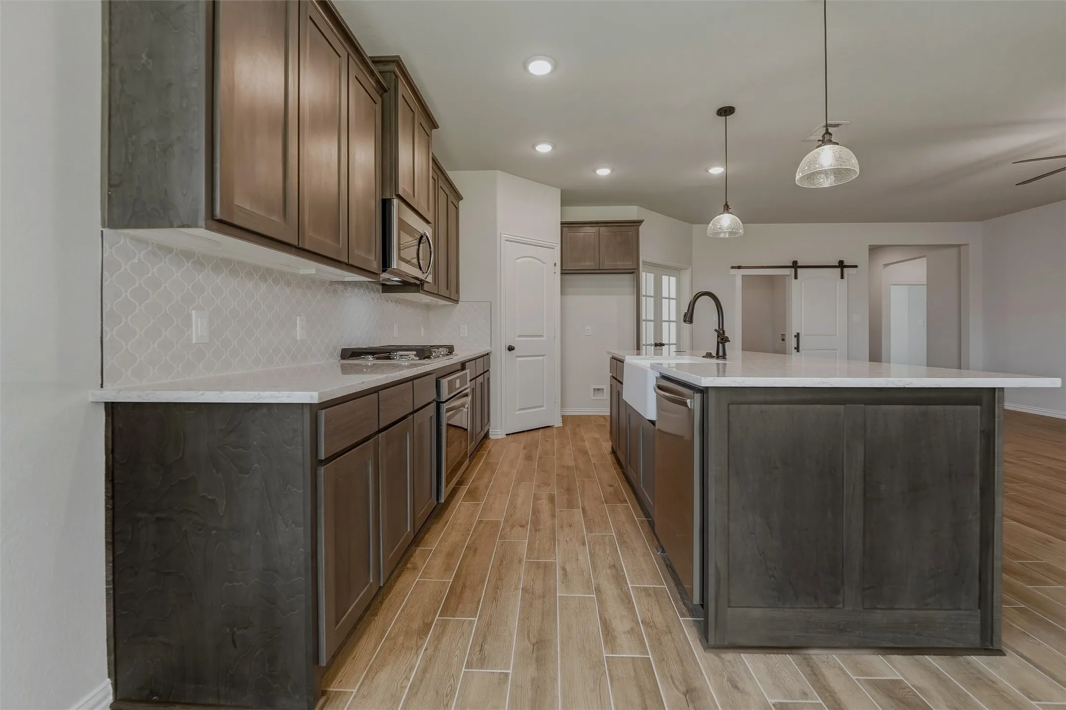 Kitchen featuring wood-finish flooring, dark wood cabinetry, light countertops, a patterned tile backsplash, and stainless steel appliances