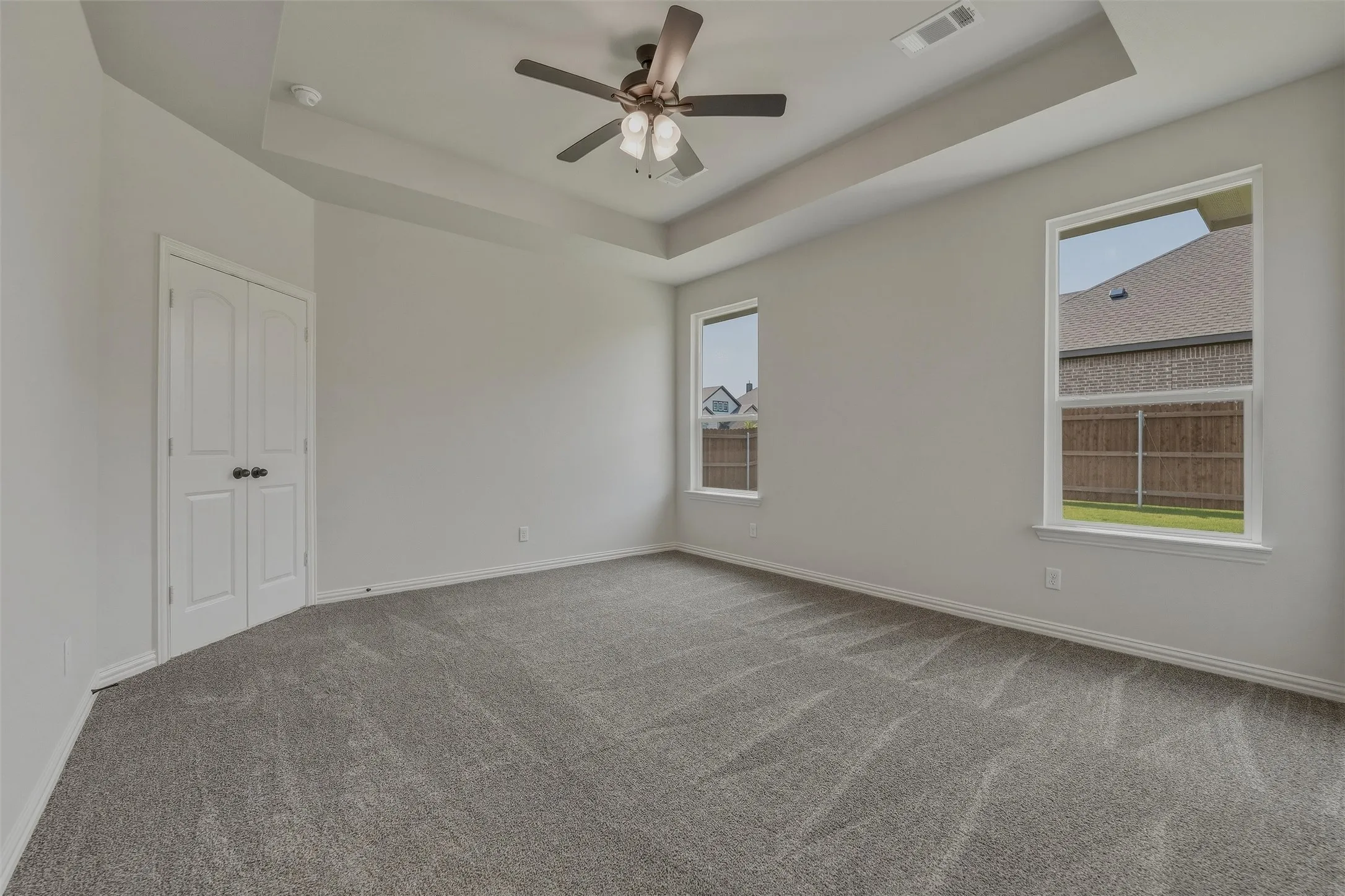 Tray ceiling with a ceiling fan, two windows, and gray carpeting