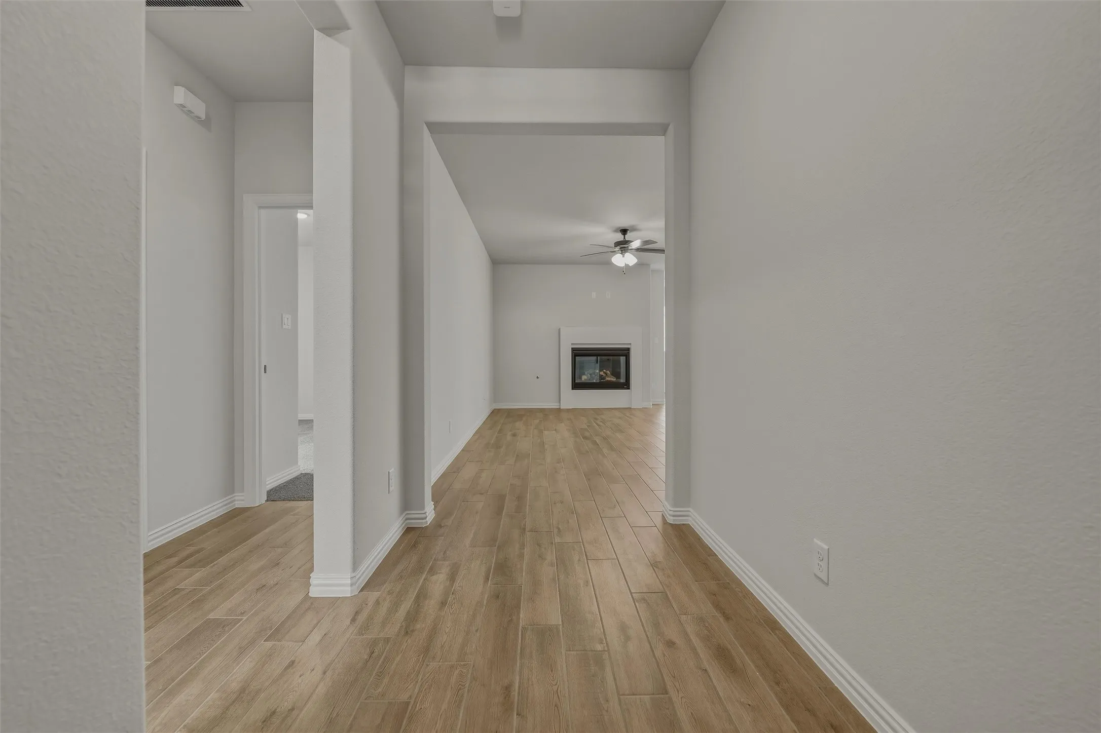 Wood-finish flooring throughout, white interior walls, and a recessed fireplace with a mantel