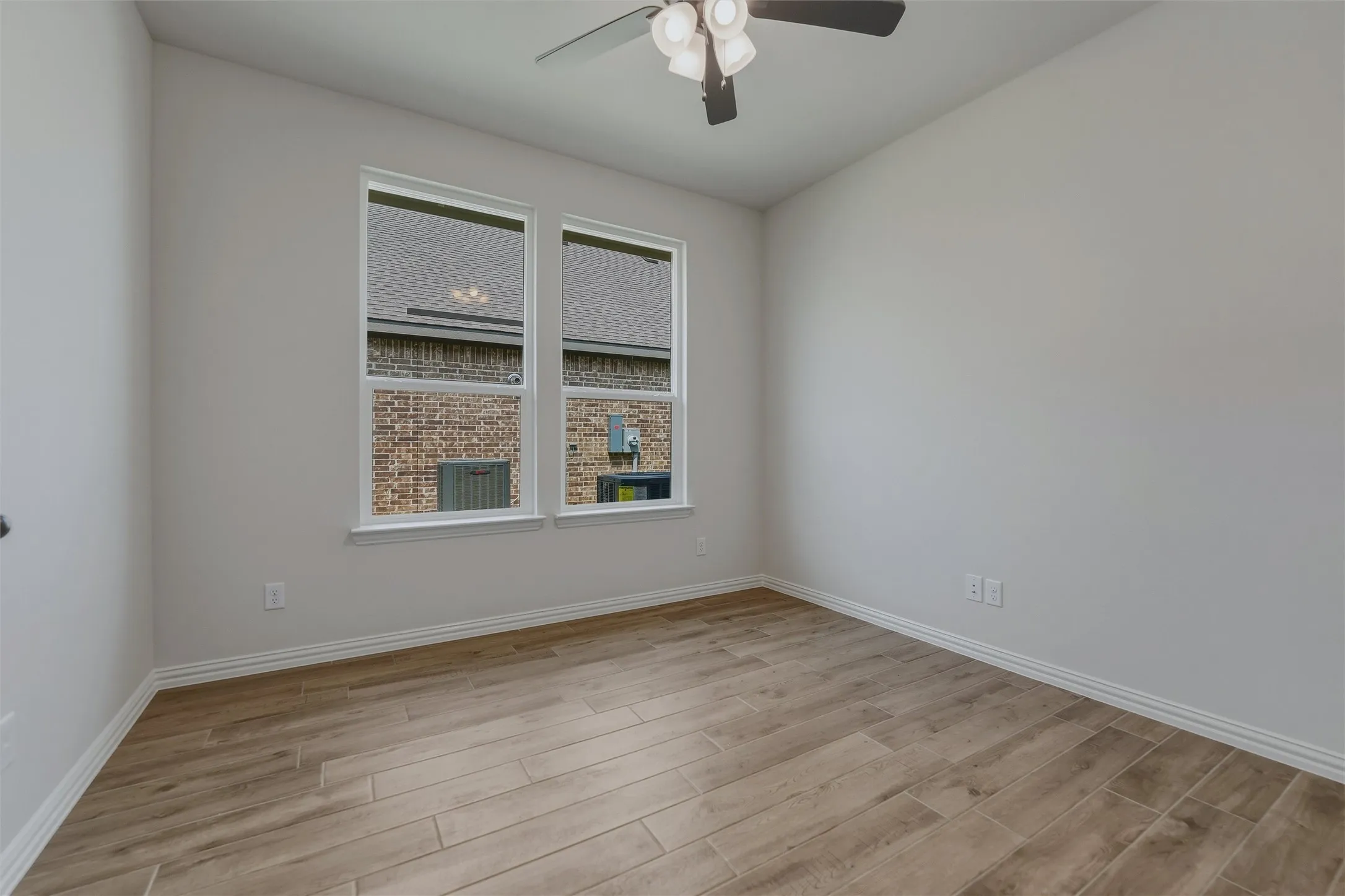 Wood-look plank flooring, light neutral wall color, white trim, dual windows, and a ceiling fan with integrated lighting