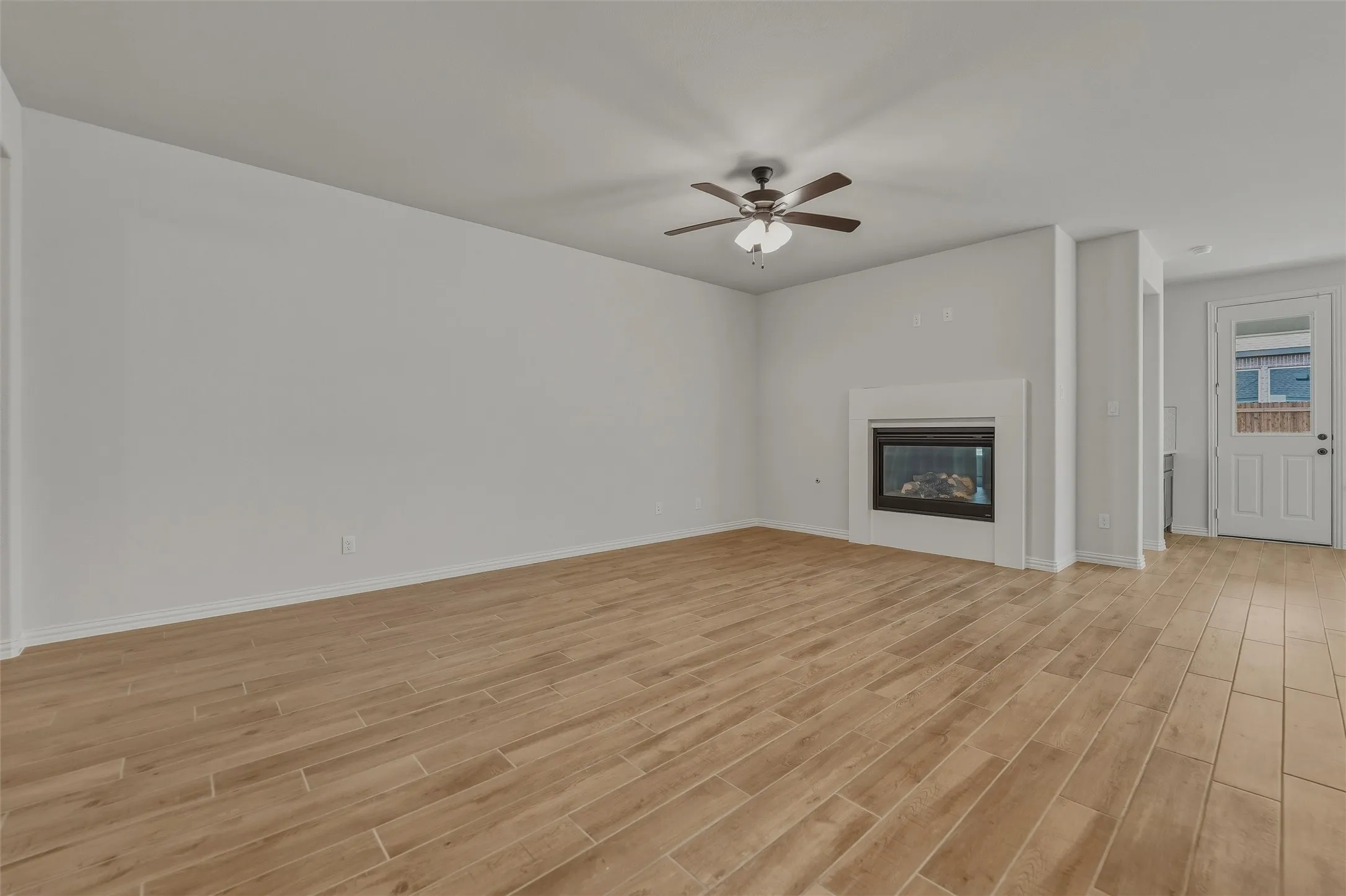 Spacious room featuring wood-look tile flooring, a modern fireplace with a white mantel, and a ceiling fan with integrated lighting