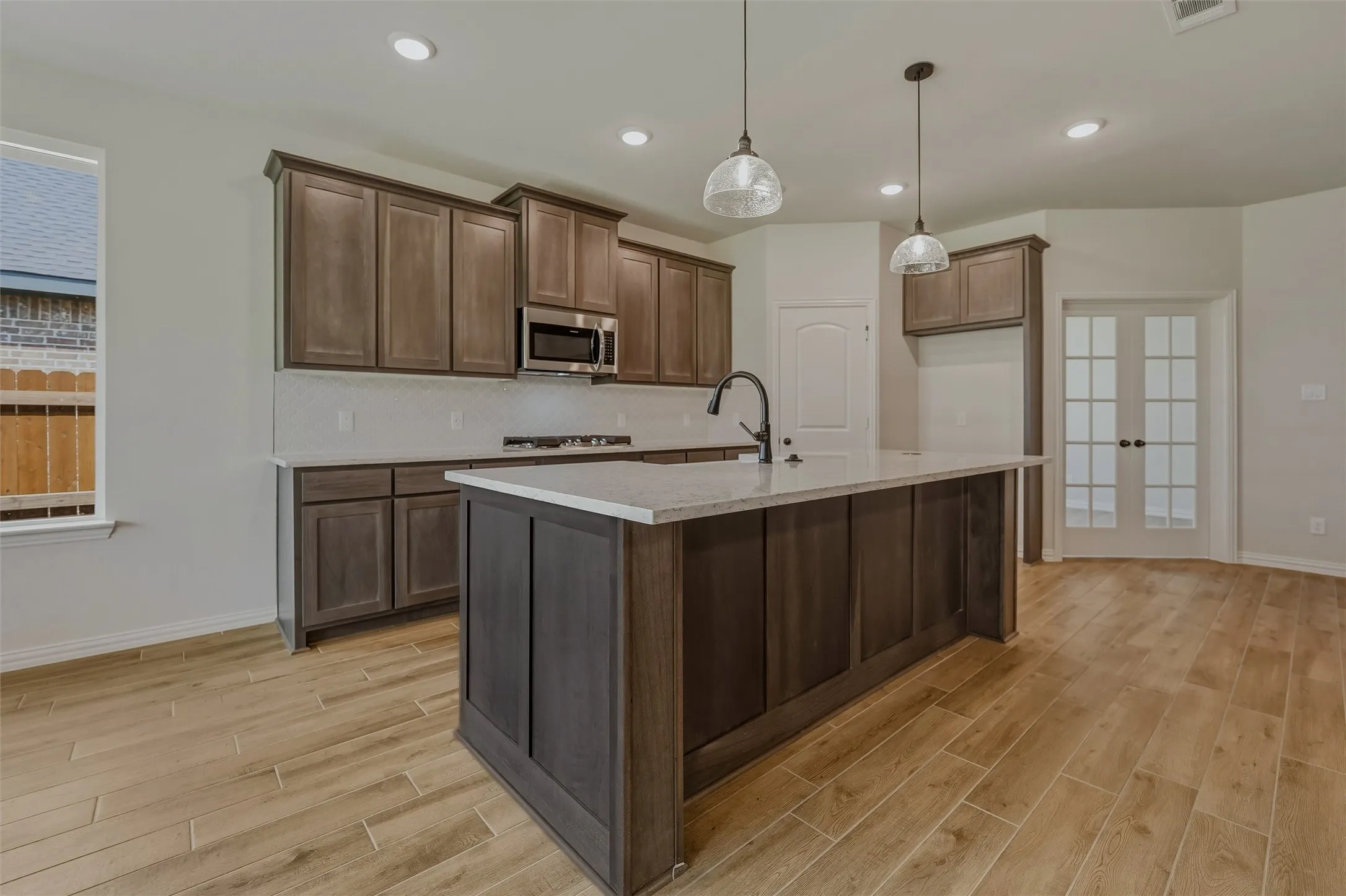Spacious kitchen featuring an island with a built-in sink, wood-finish cabinetry, light-toned countertops, and wood-finish flooring