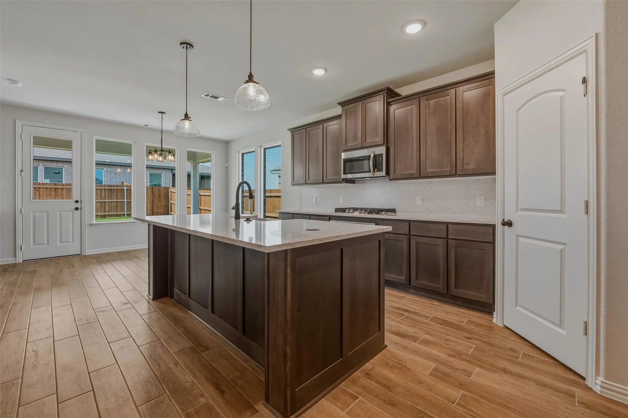 Kitchen featuring a center island with a light-toned countertop, dark wood-finish cabinetry, tile backsplash, built-in microwave, and wood-finish flooring