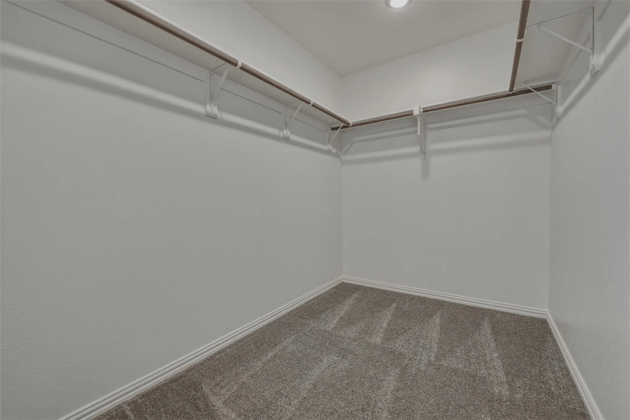 Recessed lighting illuminating a spacious walk-in closet with carpeted flooring and multiple built-in shelving and hanging rods
