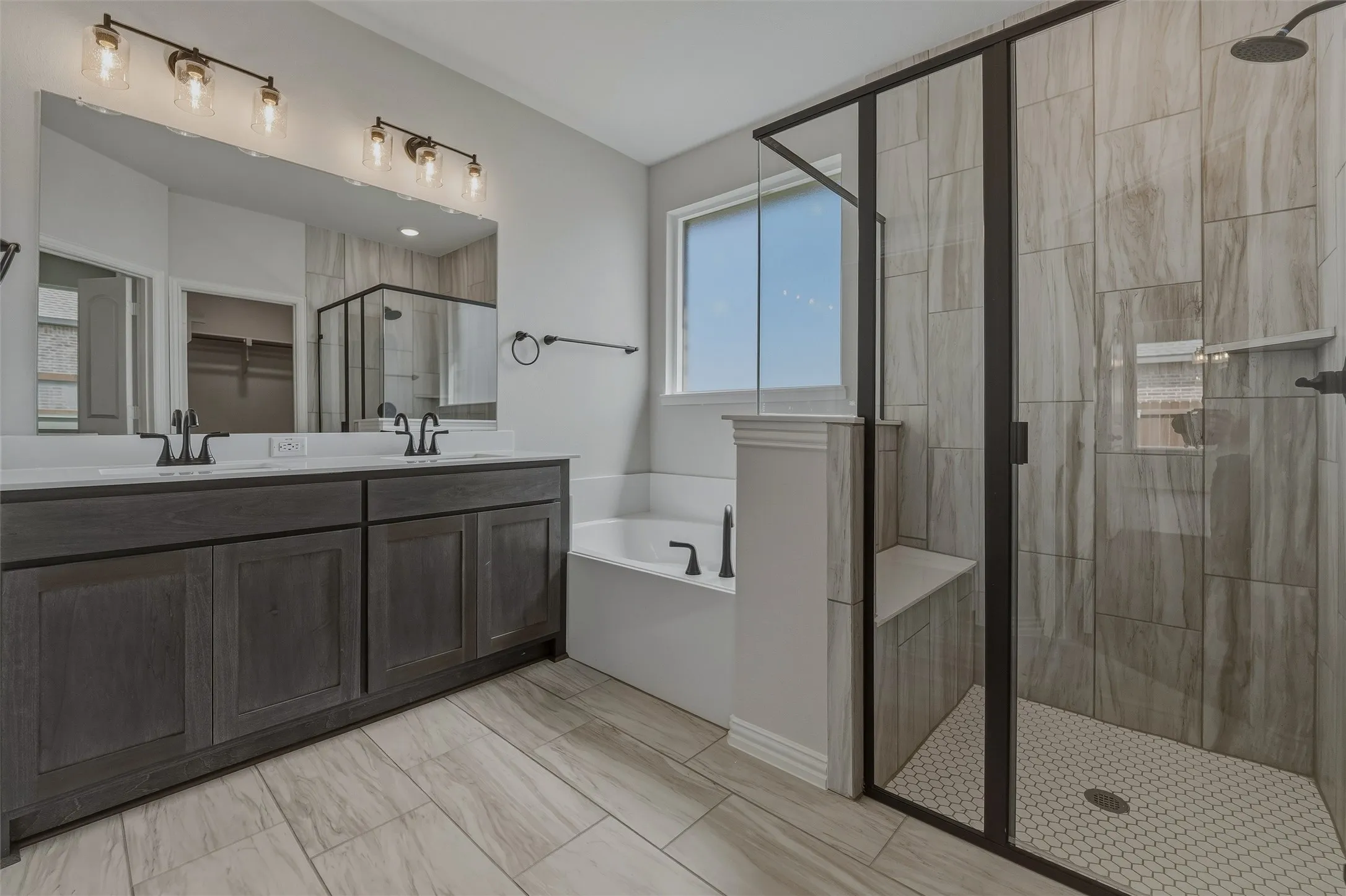 Double vanity with dark wood-finish cabinetry, built-in bathtub, glass-enclosed shower with tiled walls, and patterned tile flooring