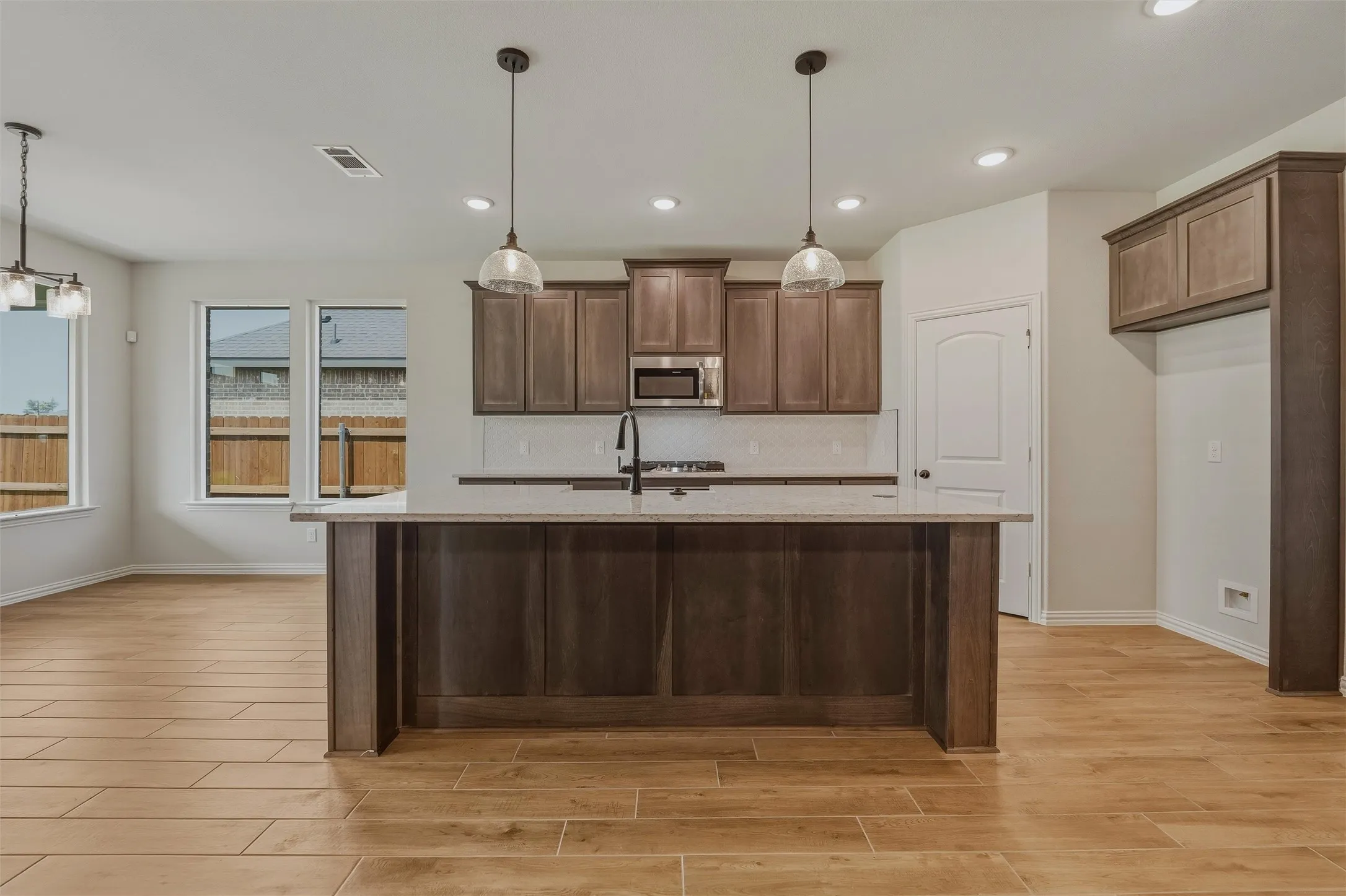Wood-finish tile flooring throughout, featuring a central kitchen island with countertop, dark wood-finish cabinetry, and recessed lighting