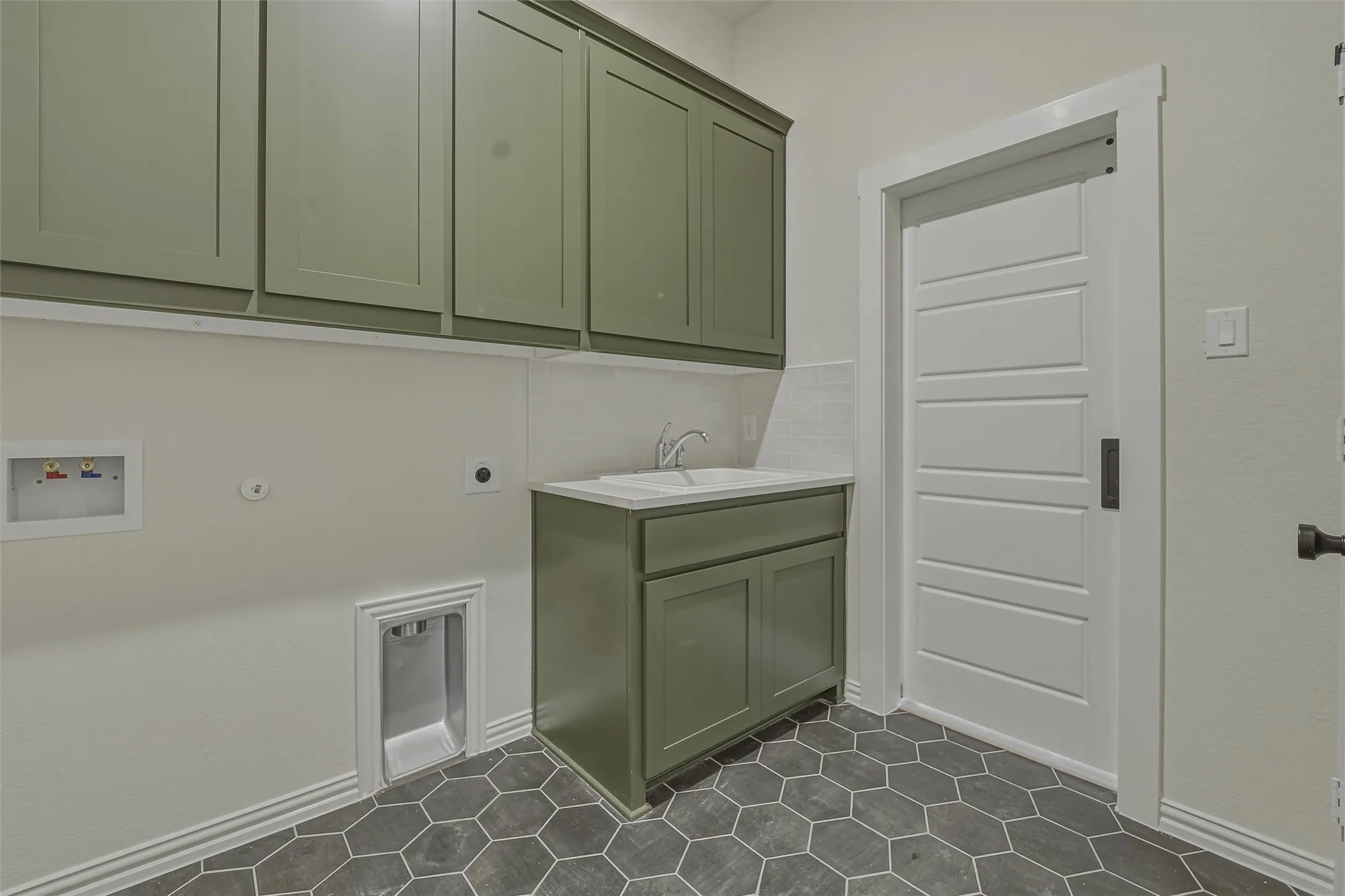 Utility room featuring a built-in sink with a white countertop, olive green cabinetry, hexagon tile flooring, and a sliding barn door